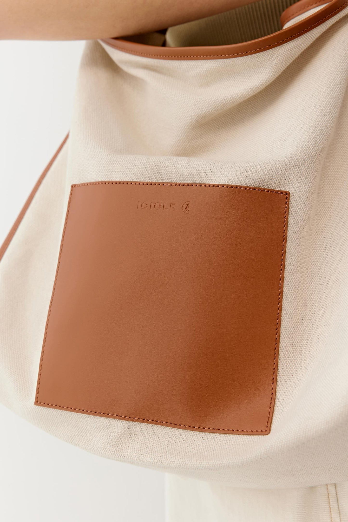 Close-up detail showing the camel leather pocket panel stitched onto the linen and cotton canvas, revealing the contrast between the smooth leather and the textured natural fabric.