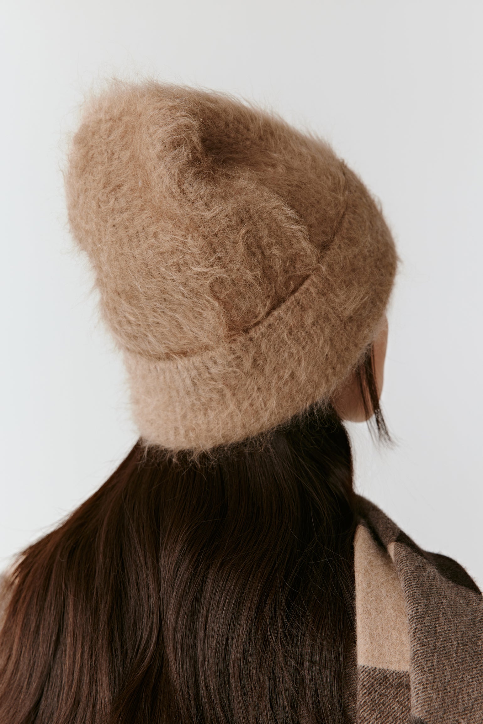 Back view of a woman wearing a taupe knit beanie and long straight hair, against a light background.