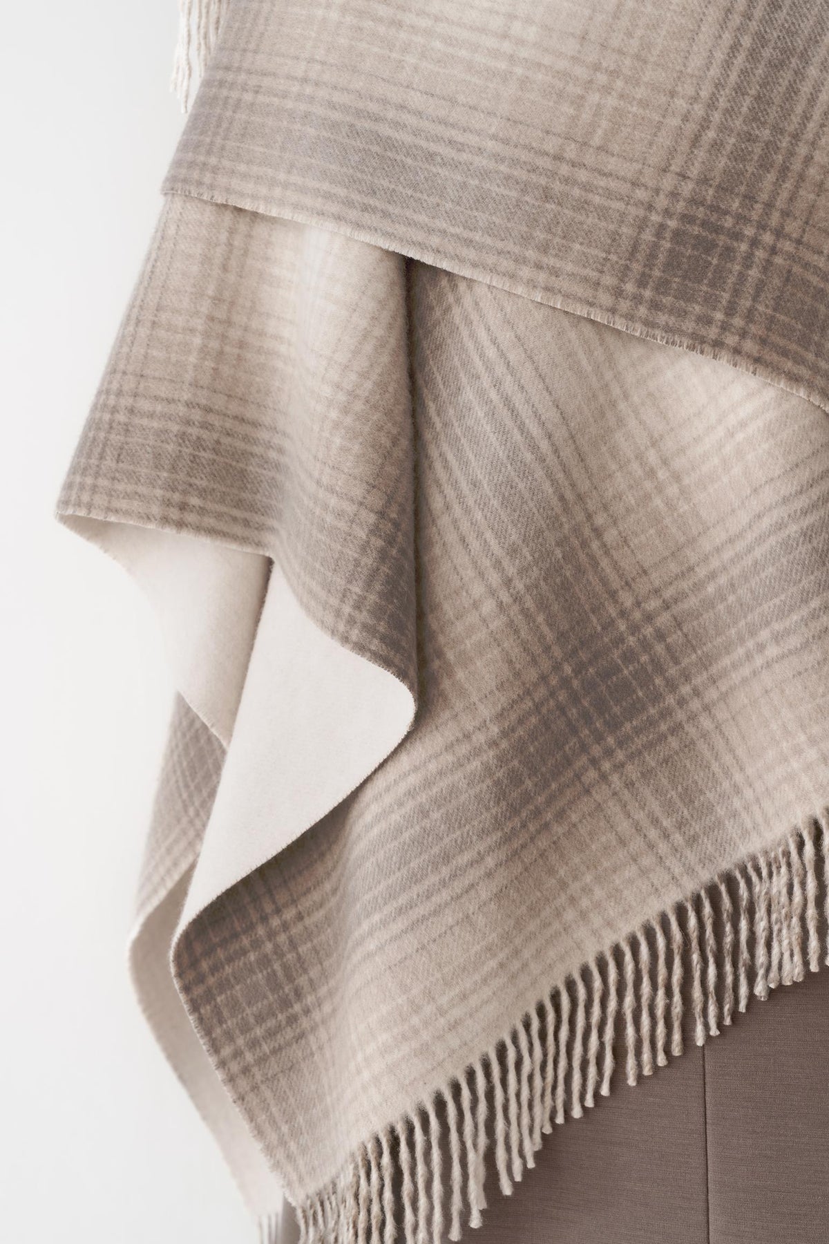 Close-up of the beige ombré shawl, highlighting the contrasting border and fringed trim.