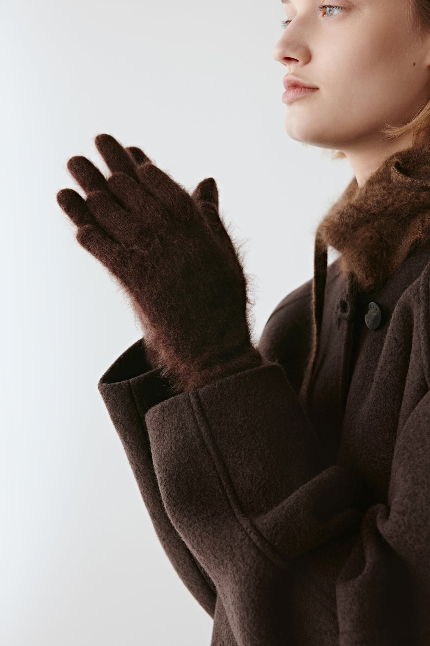 Woman wearing brown knit gloves paired with a dark wool coat on a light background