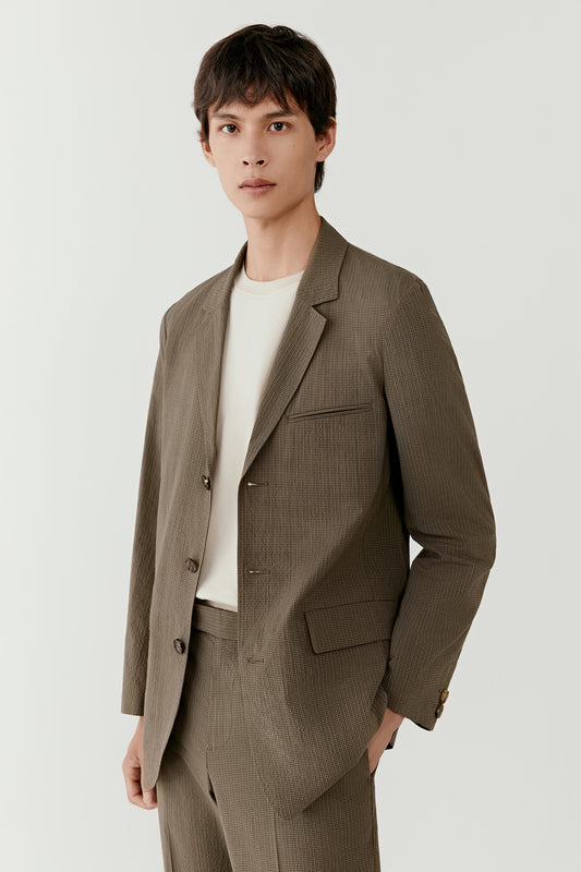 Three-quarter view showing the khaki check blazer with notch lapel and relaxed straight cut, highlighting the lightweight unlined structure.