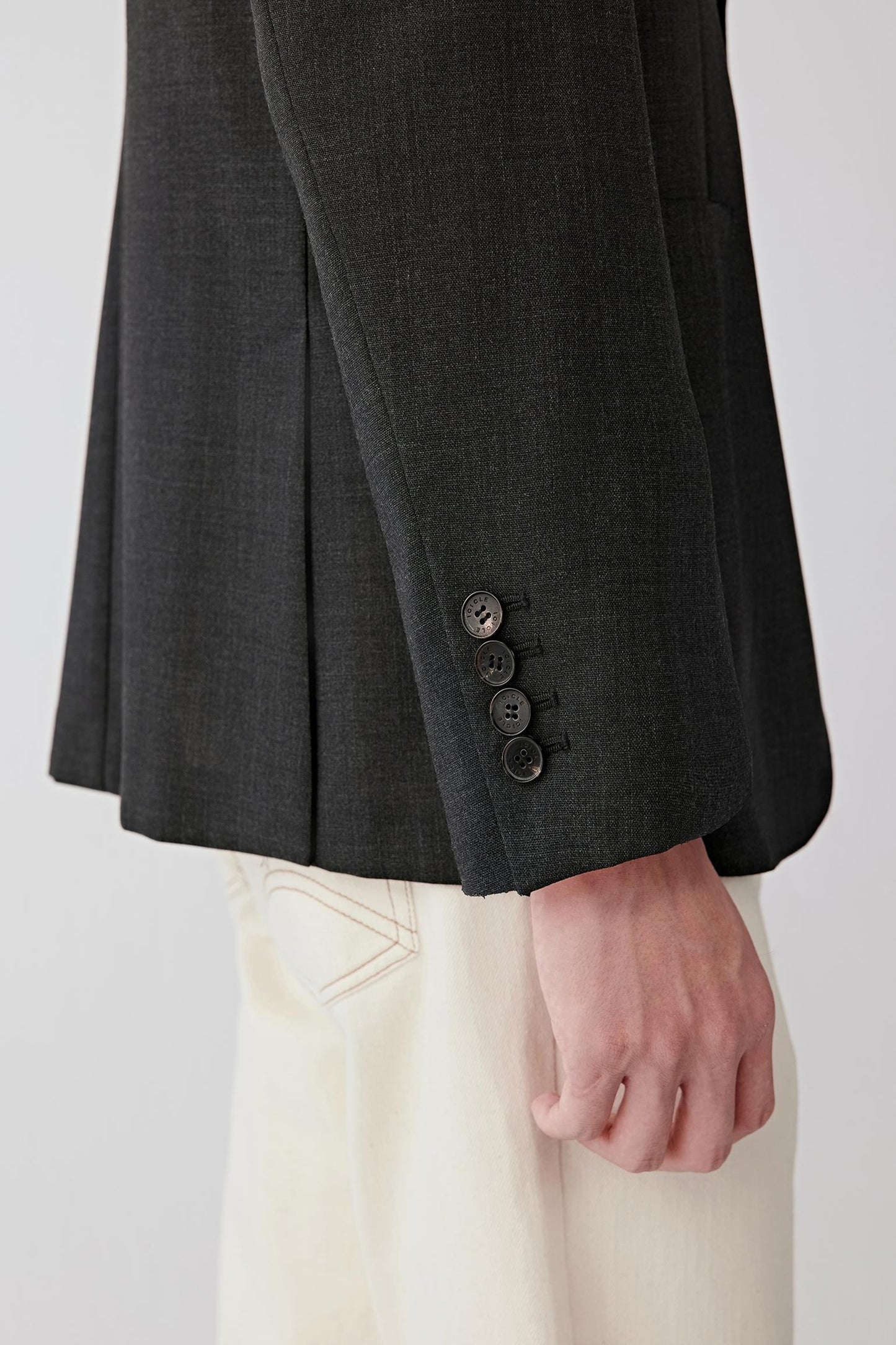 Detail of the lower front and button area, showing the discreet button fastening, sharp cut and smooth surface of the wool.