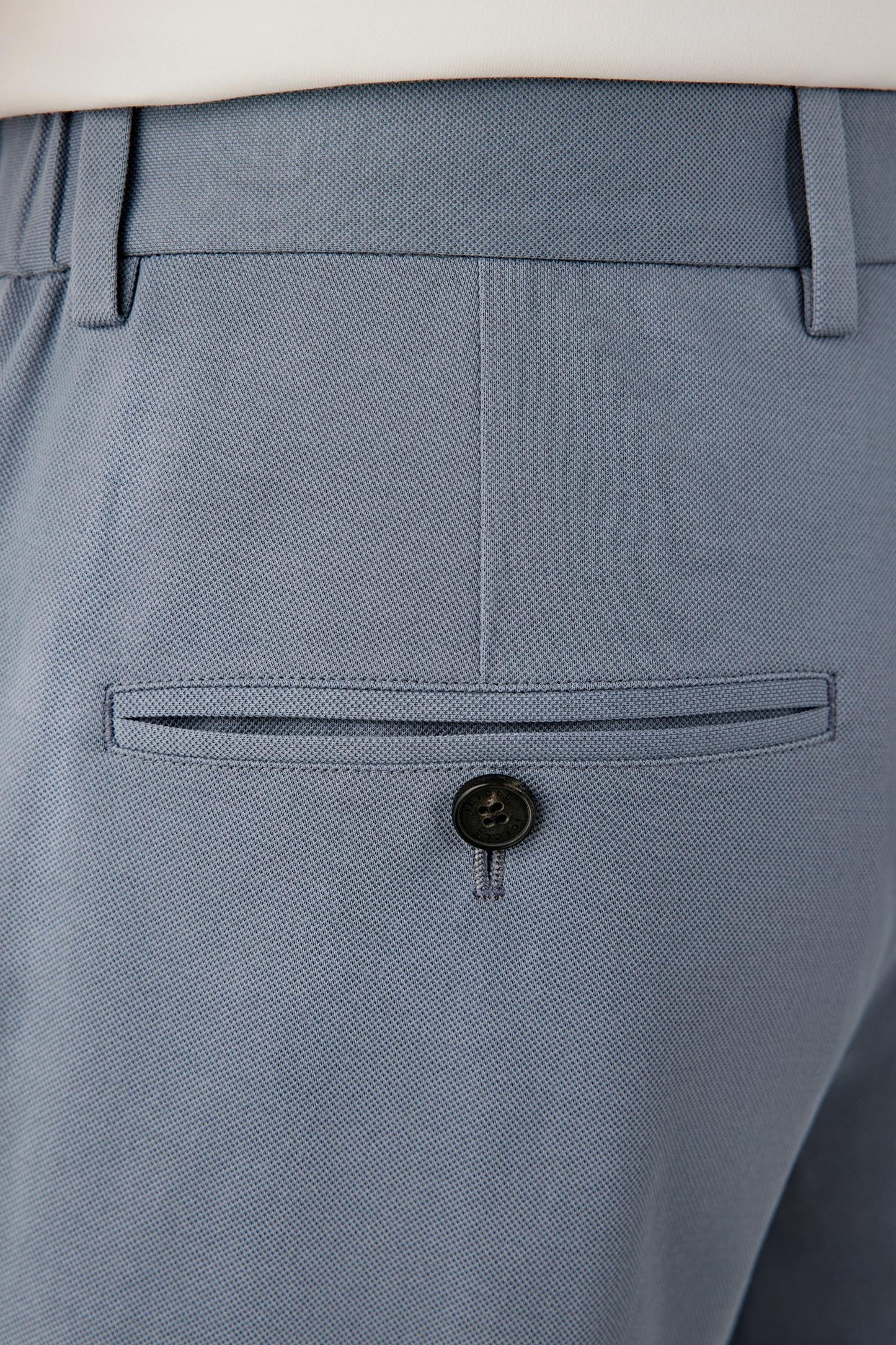 Close-up of the hem and back pocket construction showing the turned-up finish, clean stitching and subtle surface texture characteristic of cotton piqué jersey.