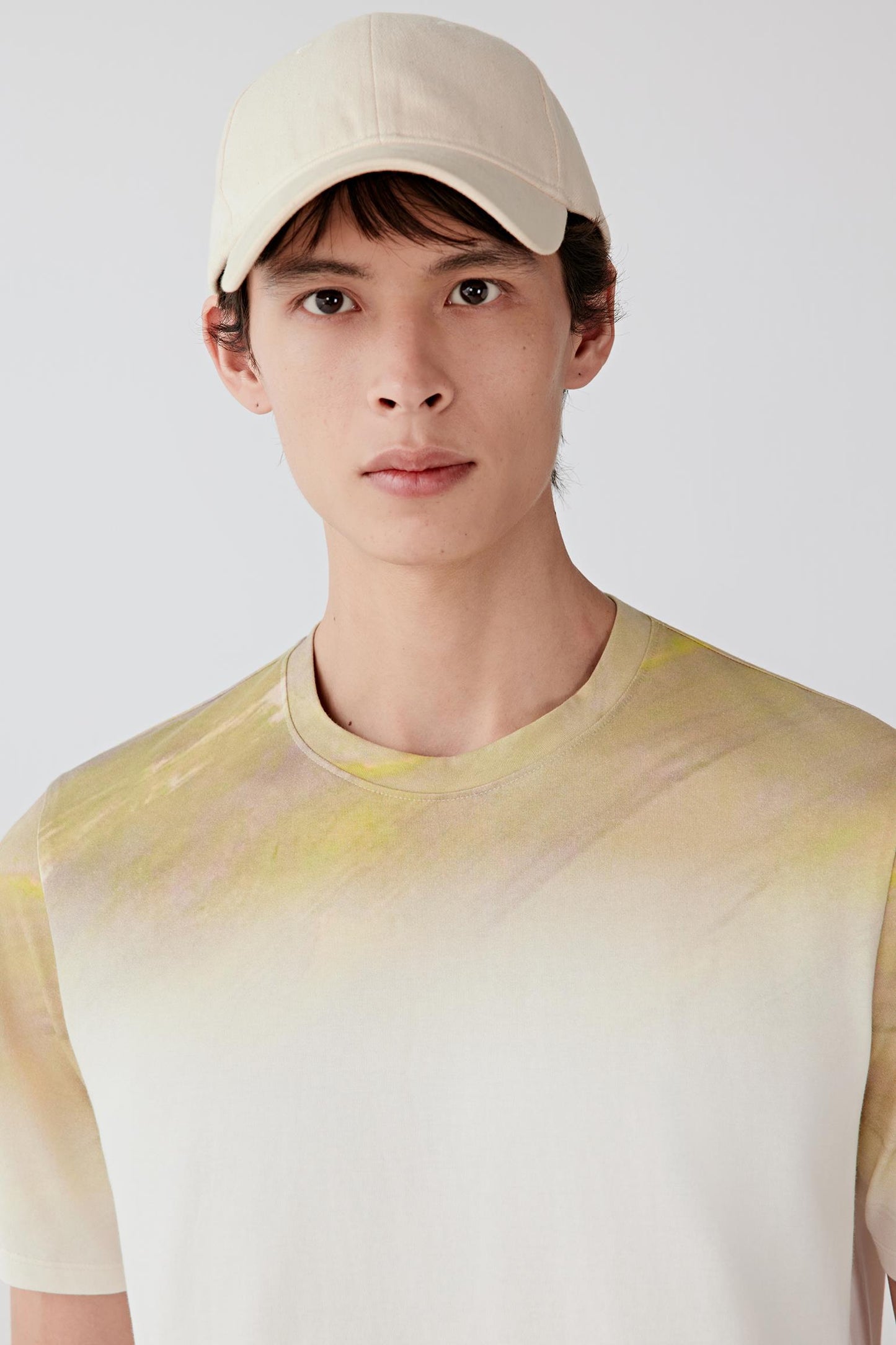 Close-up portrait focusing on the round neckline and upper construction, detailing the smooth jersey texture and soft tonal transitions between the white, yellow and beige shades.