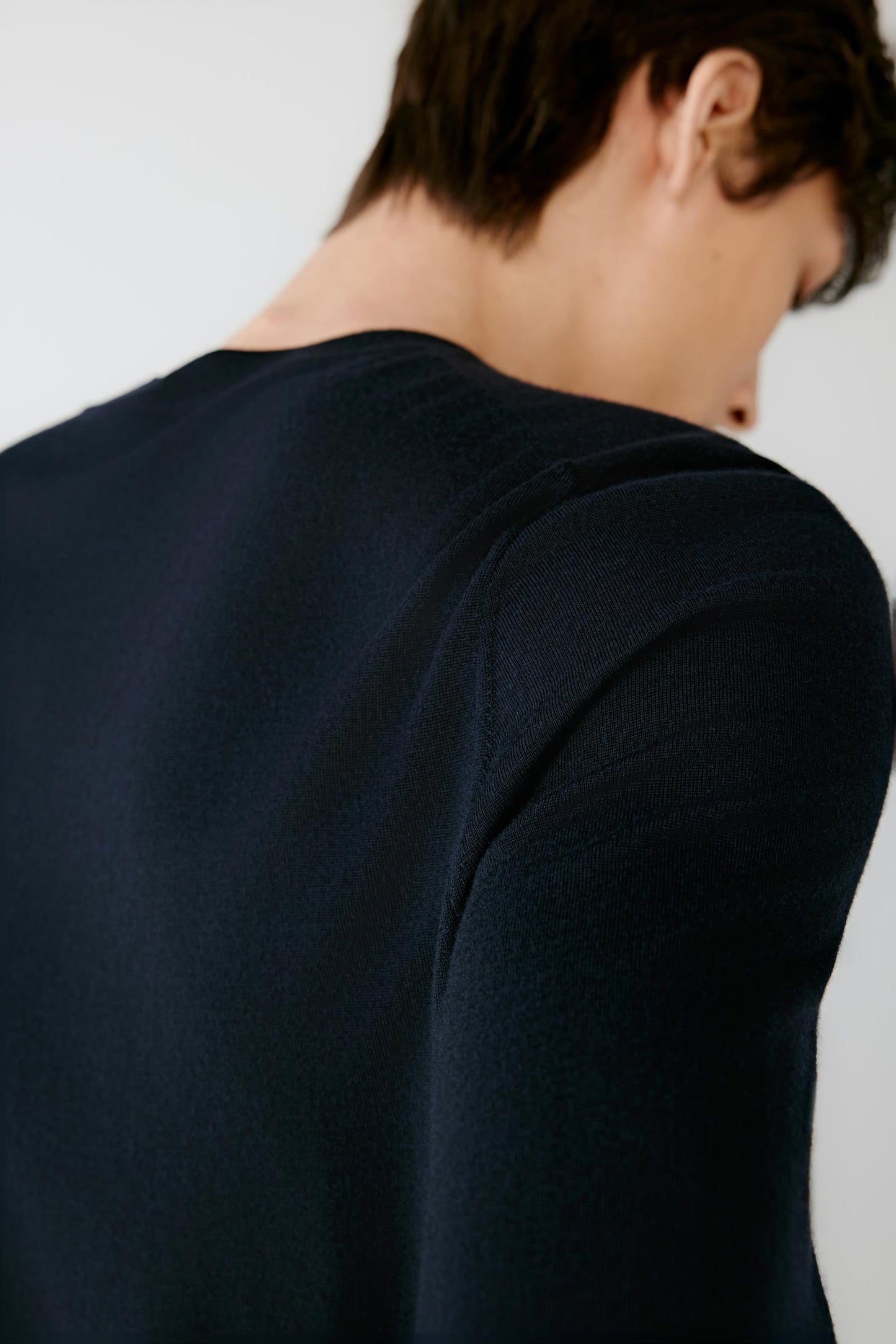 Close-up back view of a man wearing a dark navy long-sleeve knit top against a plain light background.