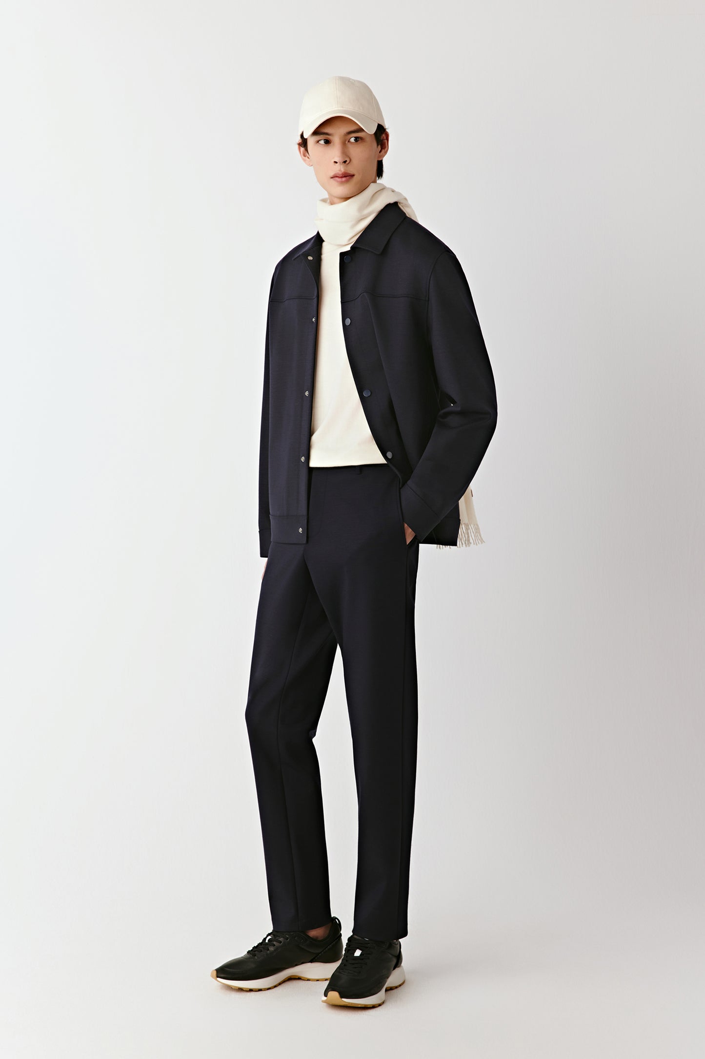 Full-length view of a man wearing navy structured wool-blend trousers with a dark jacket and beige cap, presenting a relaxed yet refined silhouette.