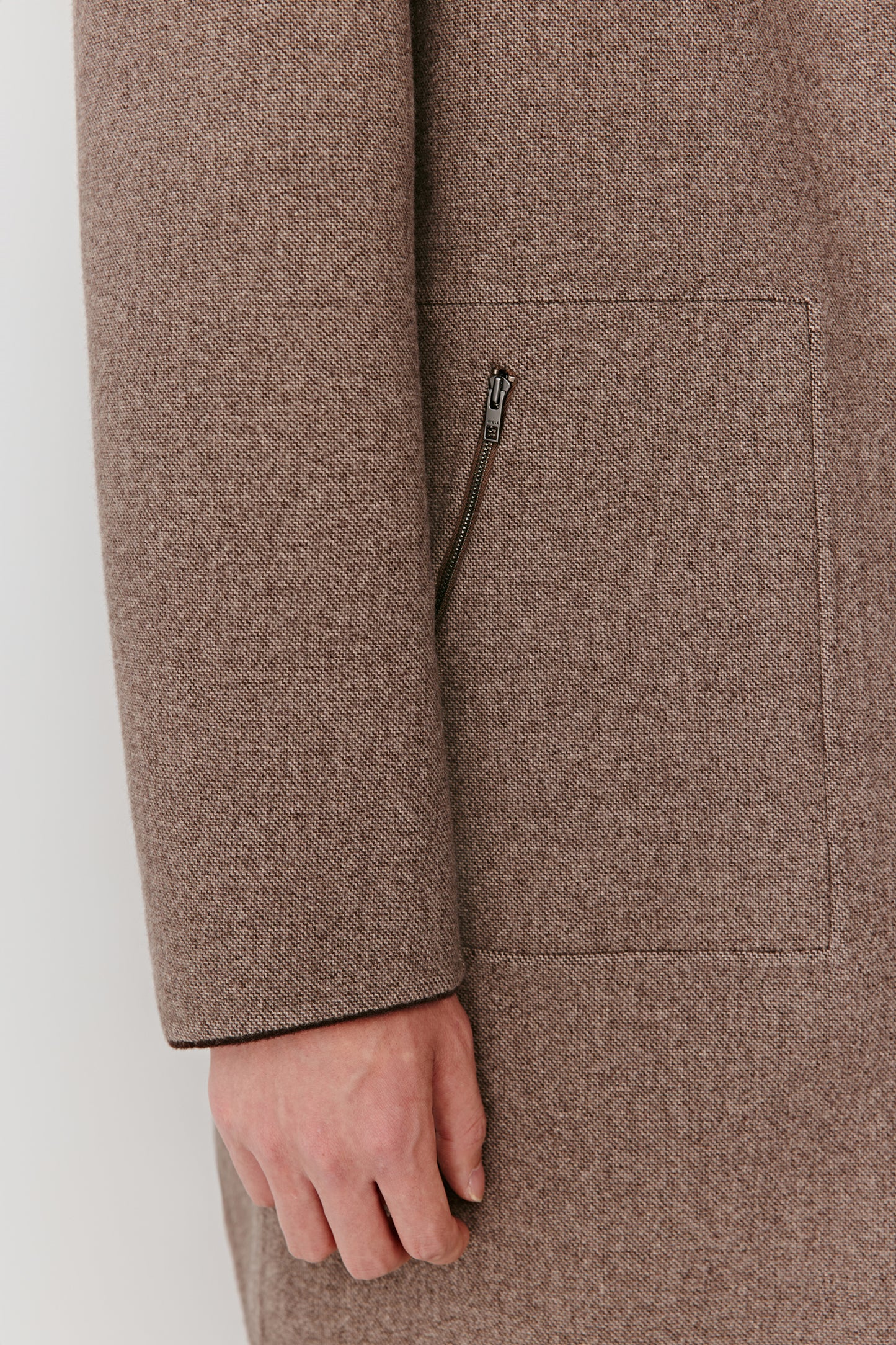 Close-up of a brown coat with a hand partially visible, on a white background