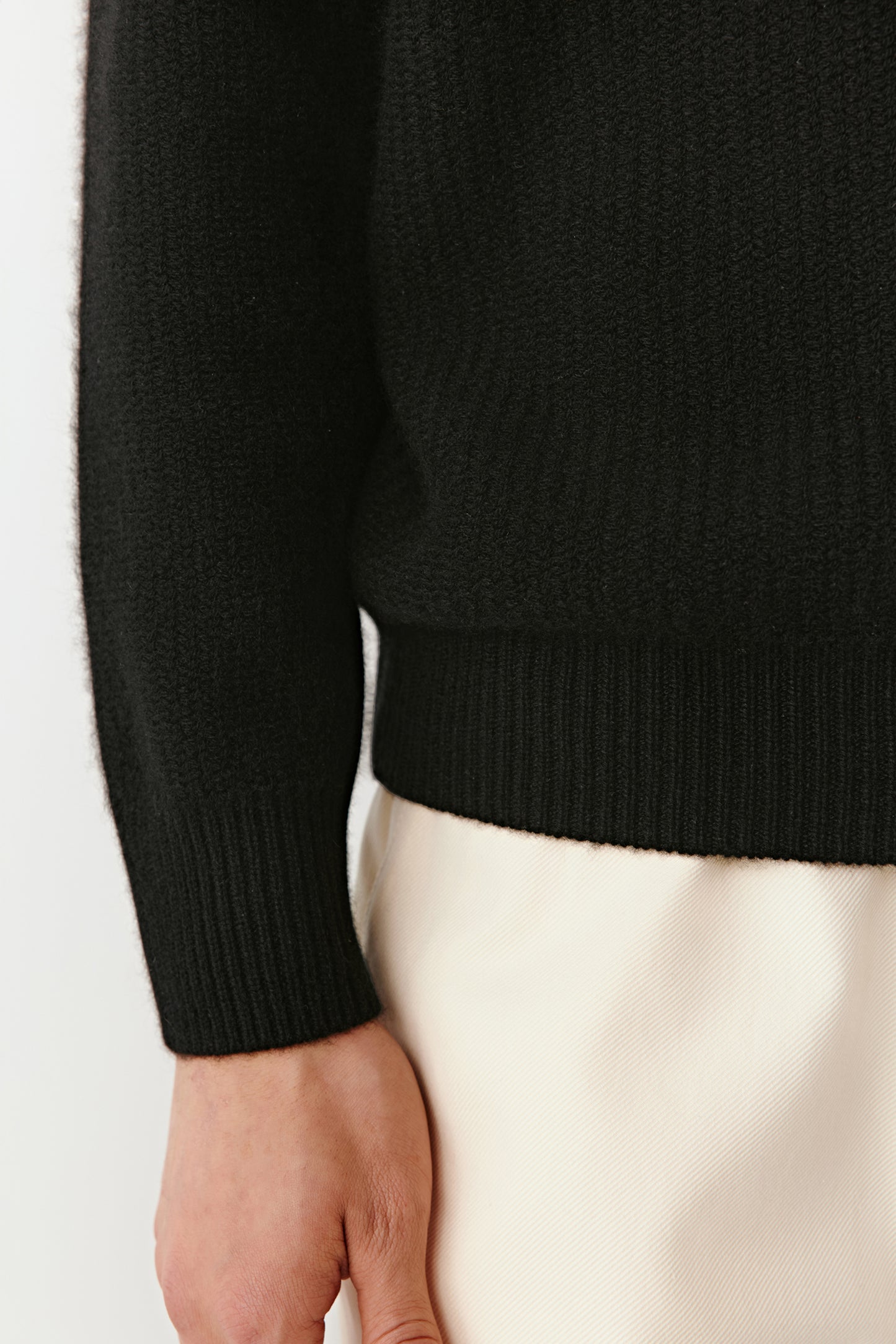 Detail close-up of the ribbed hem and sleeve cuff of the black cashmere polo sweater.