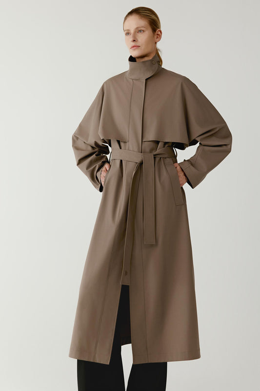 Front view showing the straight cut of the coat and the tonal belt tied at the waist. The concealed button fastening runs vertically down the front under the placket, creating a clean minimalist appearance.