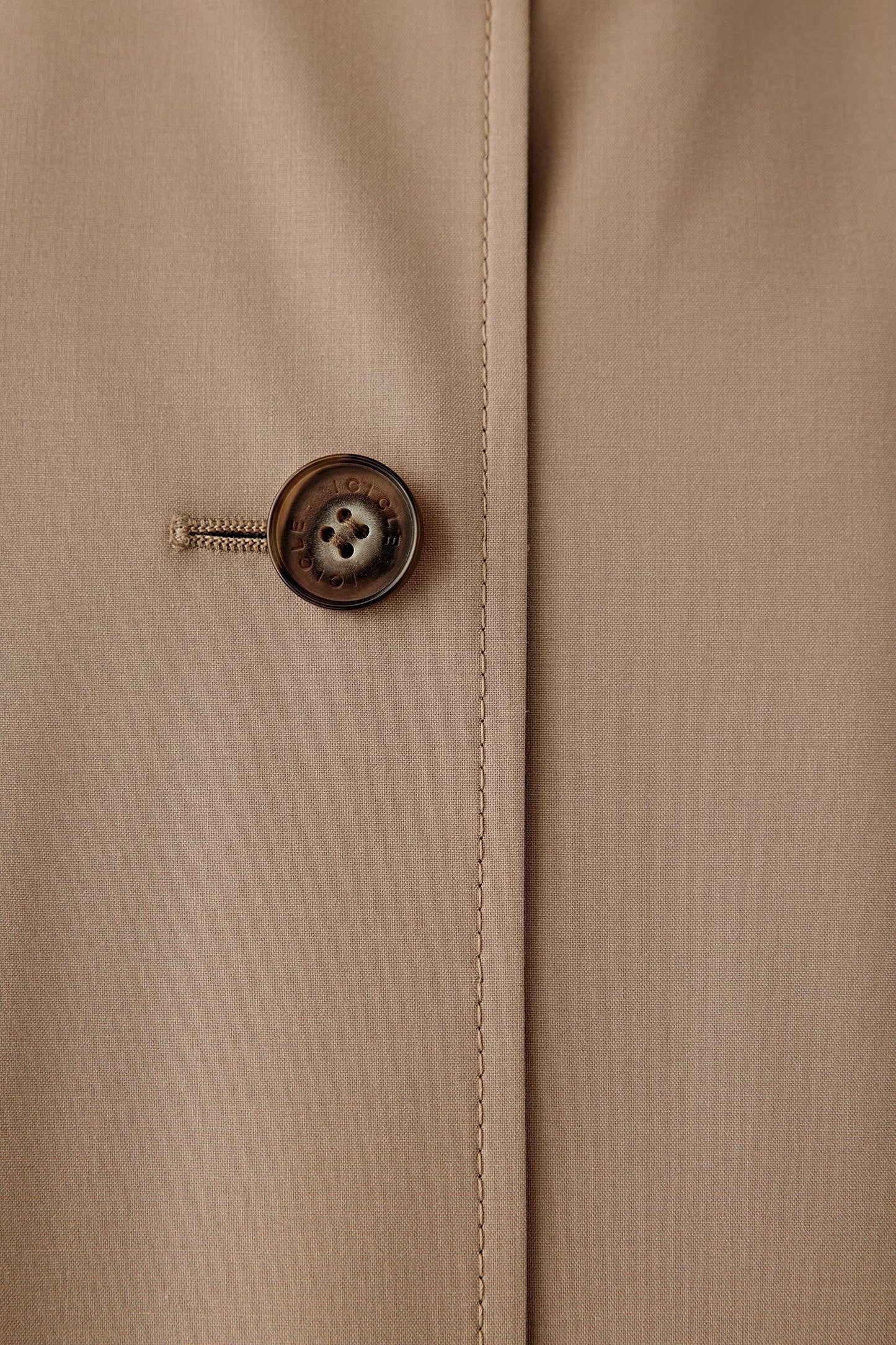 Close-up detail of the button fastening and fabric surface, showing refined finishing and tonal stitching.
