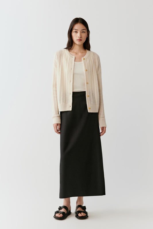 Full-length front view of a model wearing a cream cardigan knitted from a blend of cashmere and silk. The cardigan features a straight silhouette with a round neckline and a front button fastening with tonal buttons. Long sleeves extend to the wrists while the lightweight knit drapes smoothly over the torso.