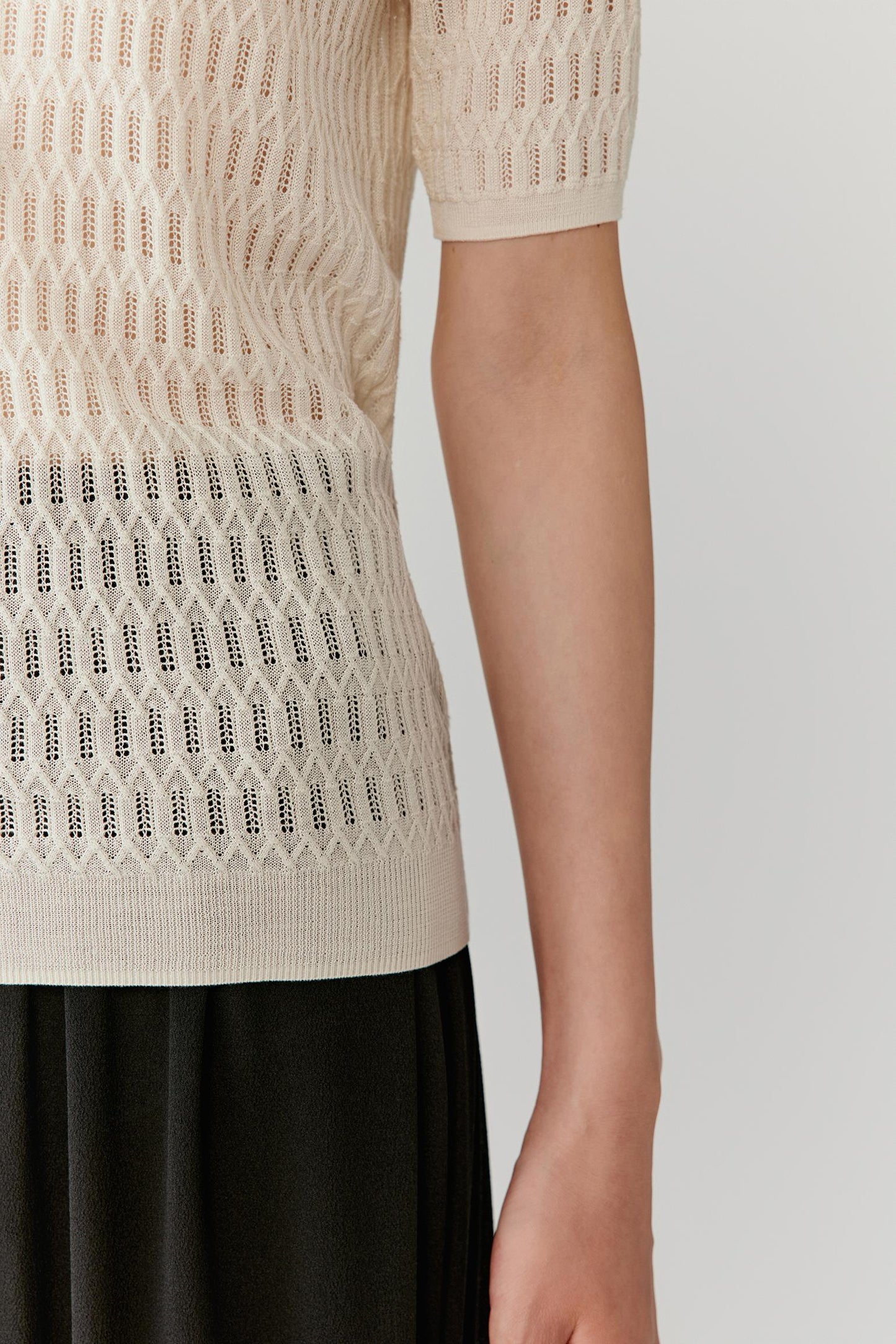 Detail of the hem and sleeve, highlighting the clean edges, lightweight construction and slightly sheer effect of the knit.