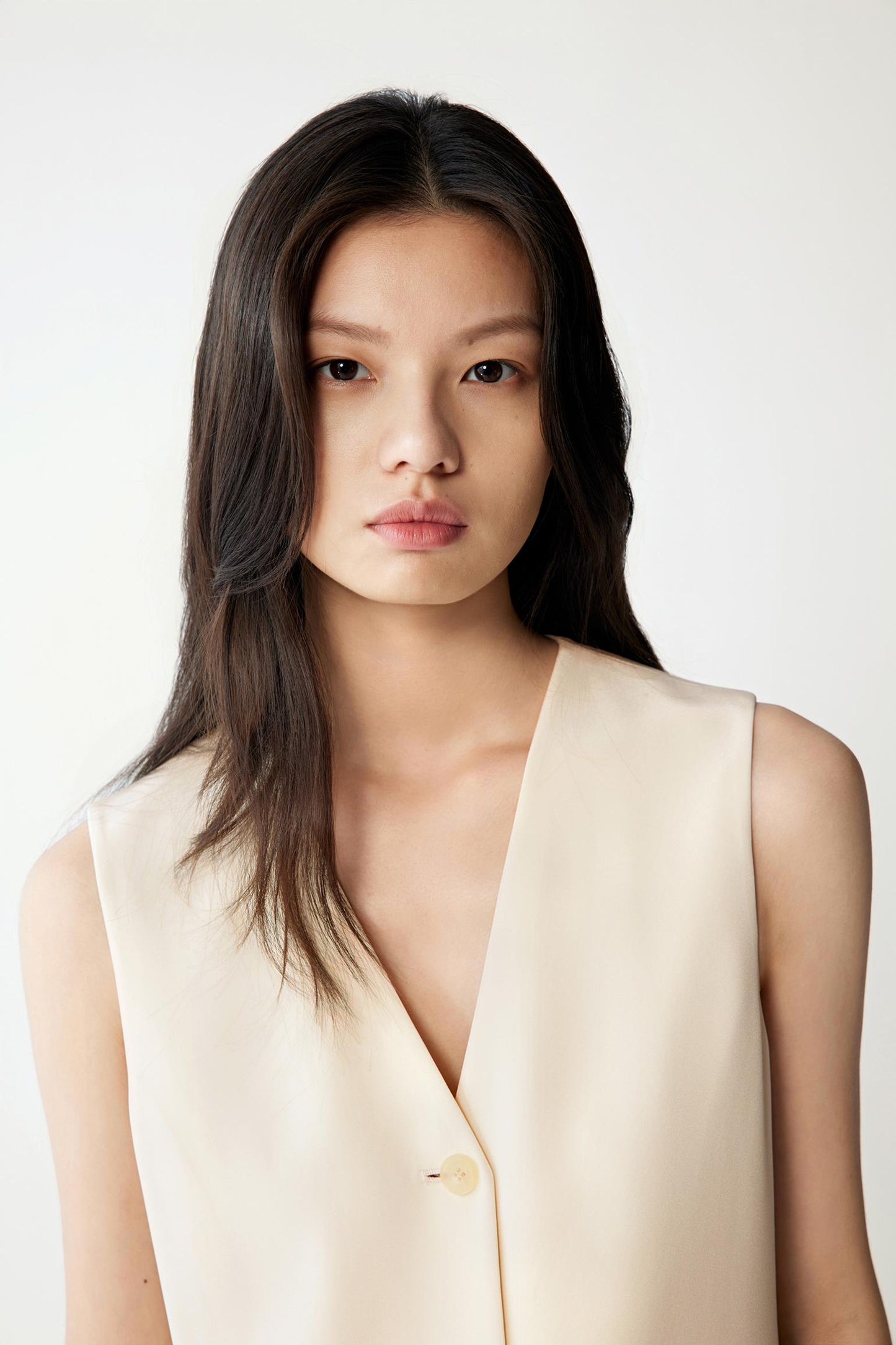 Close-up of the V-neckline and upper chest, highlighting the refined lapel-less construction, small tonal buttons and fluid structure of the silk crepe fabric.