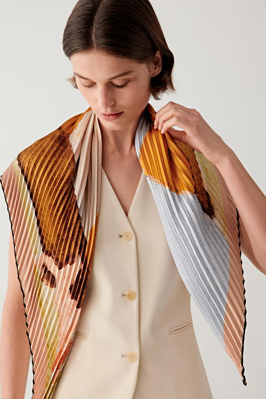 Three-quarter view showing the scarf styled around the neck with layered folds. The graphic composition becomes visible across the fabric as the scarf falls naturally over a light vest and denim trousers.