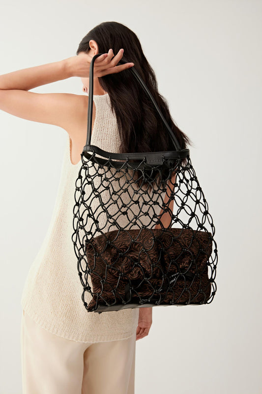 Side view showing the black leather net bag worn on the shoulder, emphasizing the flexible mesh structure, leather handles and slouchy shape.