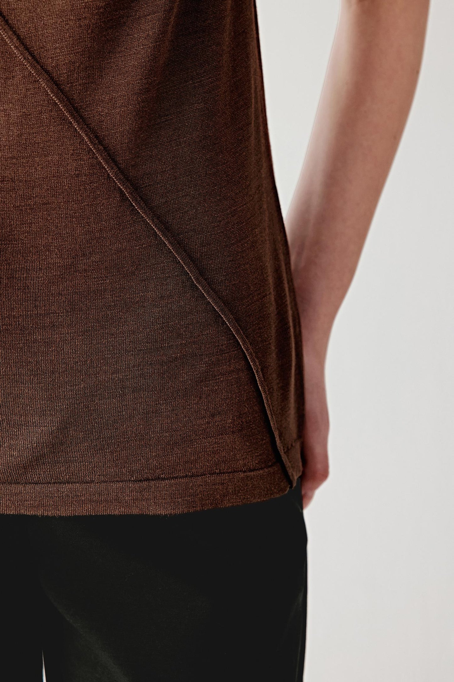 Close-up of the side and hem area, showing the diagonal seam construction, the way the fabric overlaps and the fine knit texture, emphasizing fluidity, lightness and continuity in the garment’s structure
