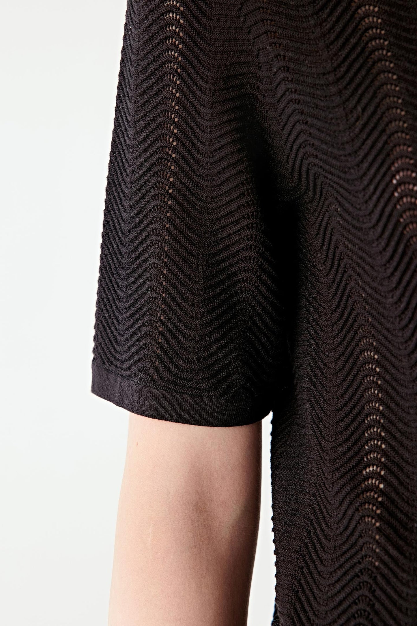 Close-up of the sleeve, showing the short sleeve cut, clean edge finish and the knit structure with its slightly sheer, breathable quality