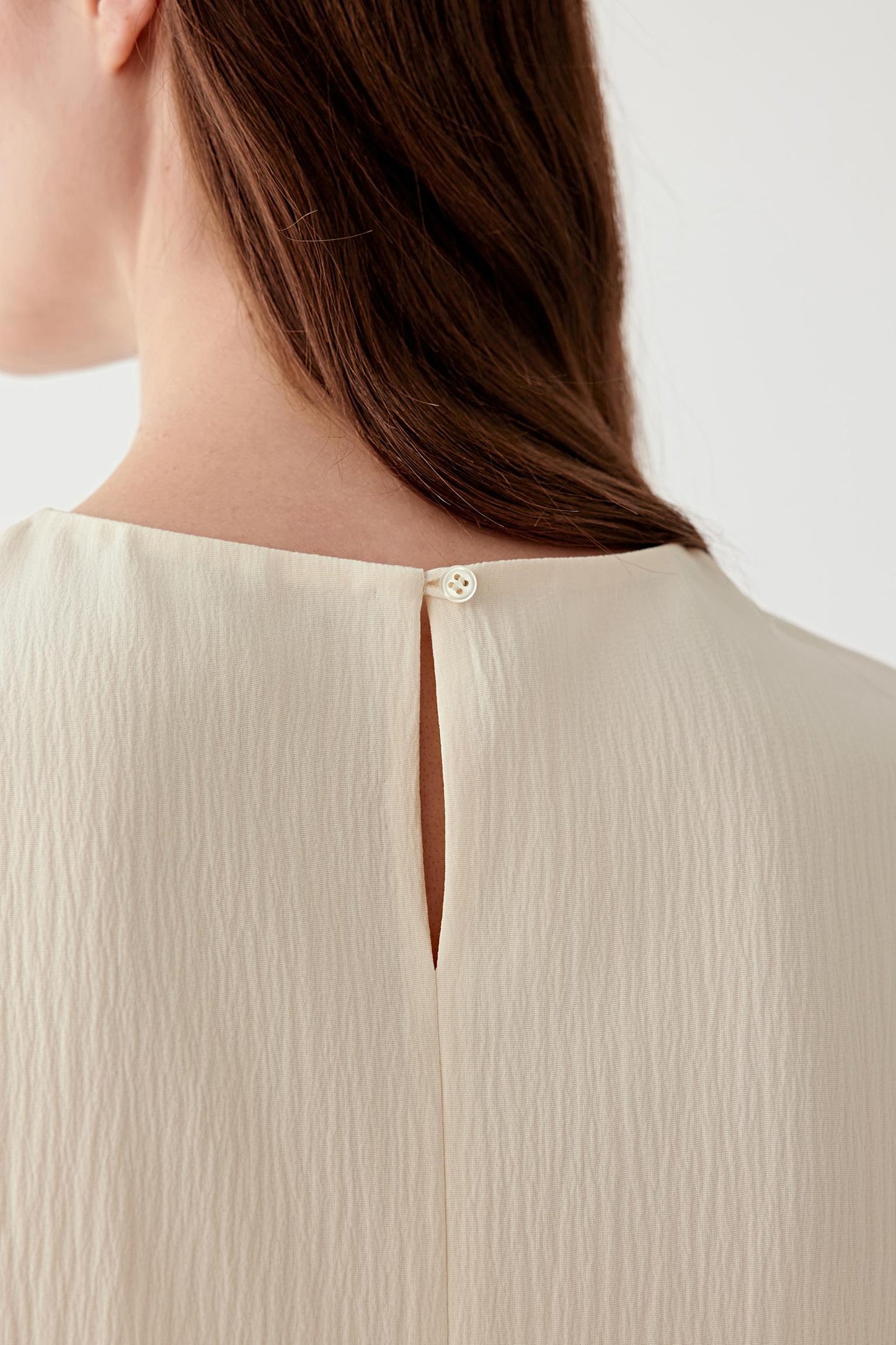 Close-up of the back neckline, focusing on the slit opening with single button fastening, showing construction detail and the delicate finish at the back