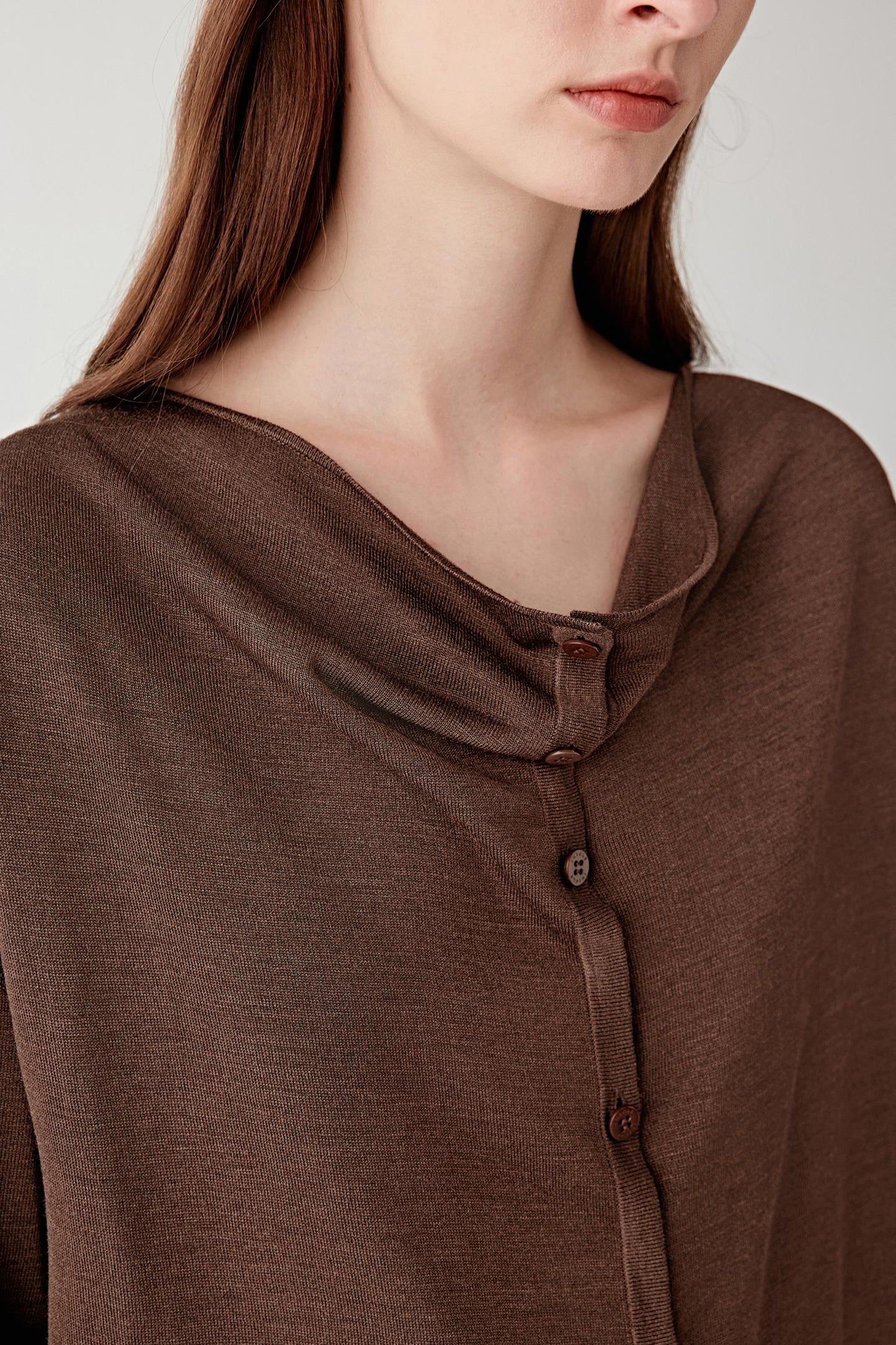 Close-up of the neckline and chest area, focusing on the draped collar, button placket detail and the subtly irregular, textured surface of the tussah silk knit, revealing depth and natural variation in the yarn