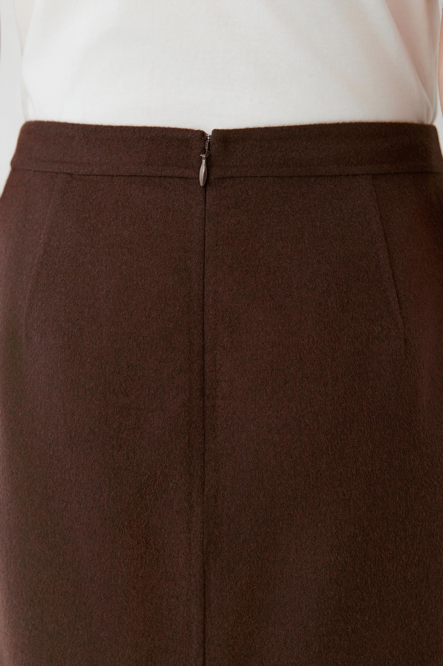 Close-up of the concealed back zip and waistband of a brown midi skirt.