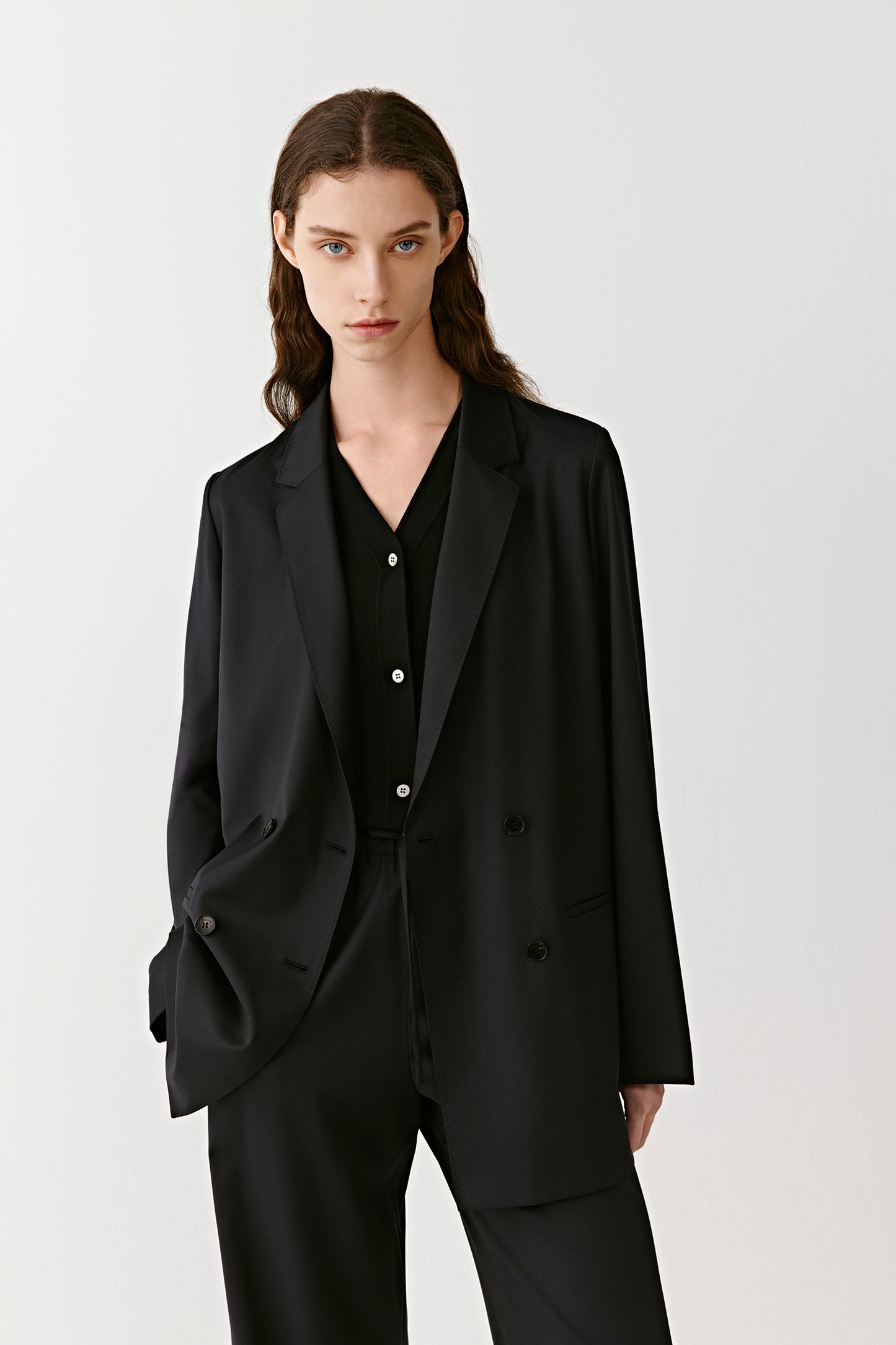 A woman stands in a black worsted wool double-breasted jacket, styled with matching trousers, against a pale background.