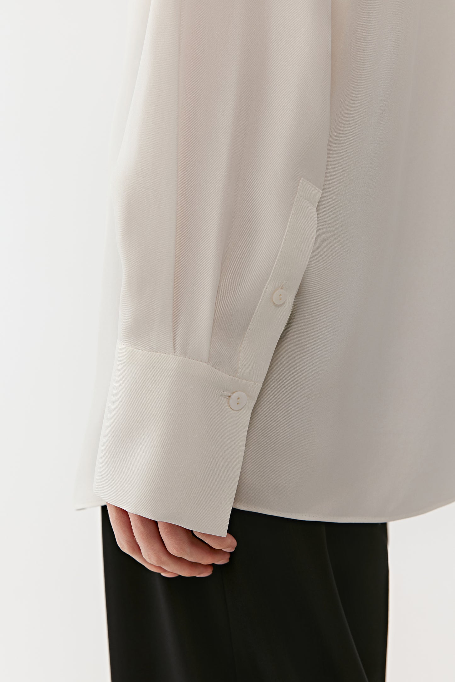 A close-up focuses on the sleeve cuff and fabric fold, revealing delicate craftsmanship.