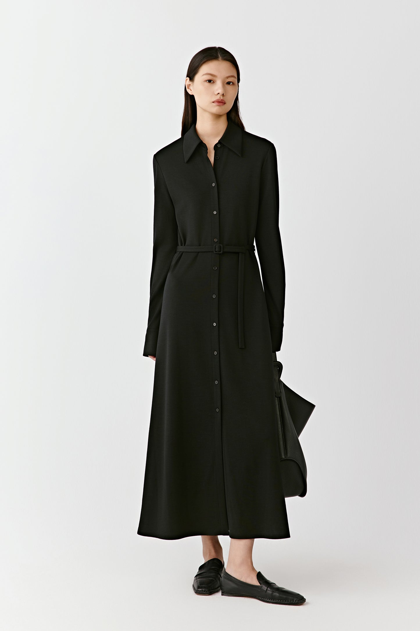 A woman stands in a black long shirt dress in combed wool jersey, the fabric flowing softly to the floor.