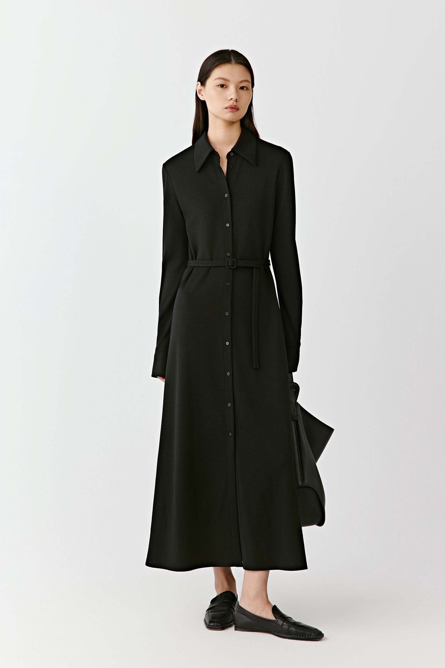 A woman stands in a black long shirt dress in combed wool jersey, the fabric flowing softly to the floor.