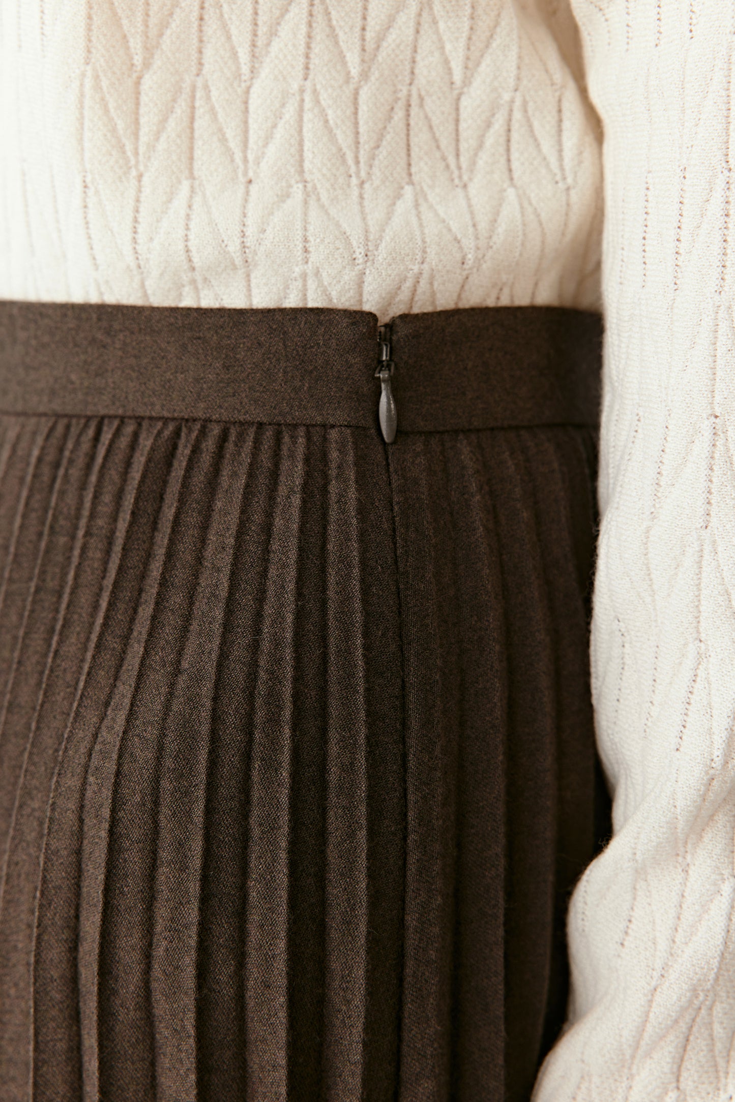 A close-up focuses on the waistband and fine pleating detail.