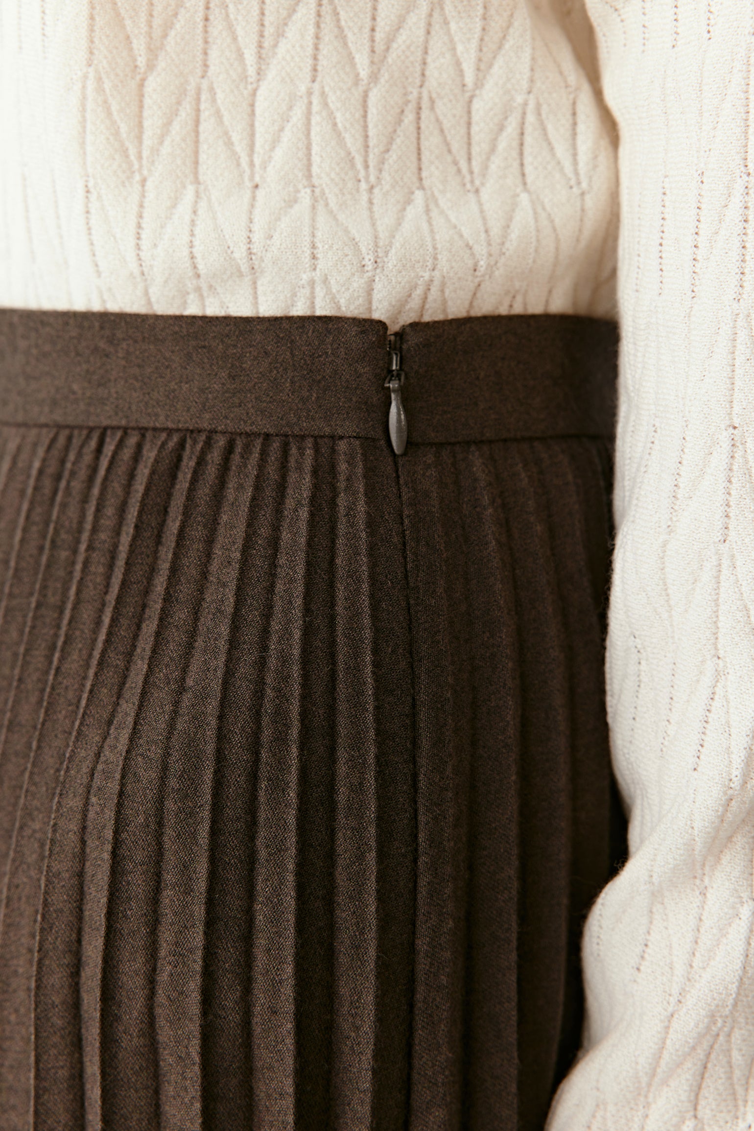 A close-up focuses on the waistband and fine pleating detail.