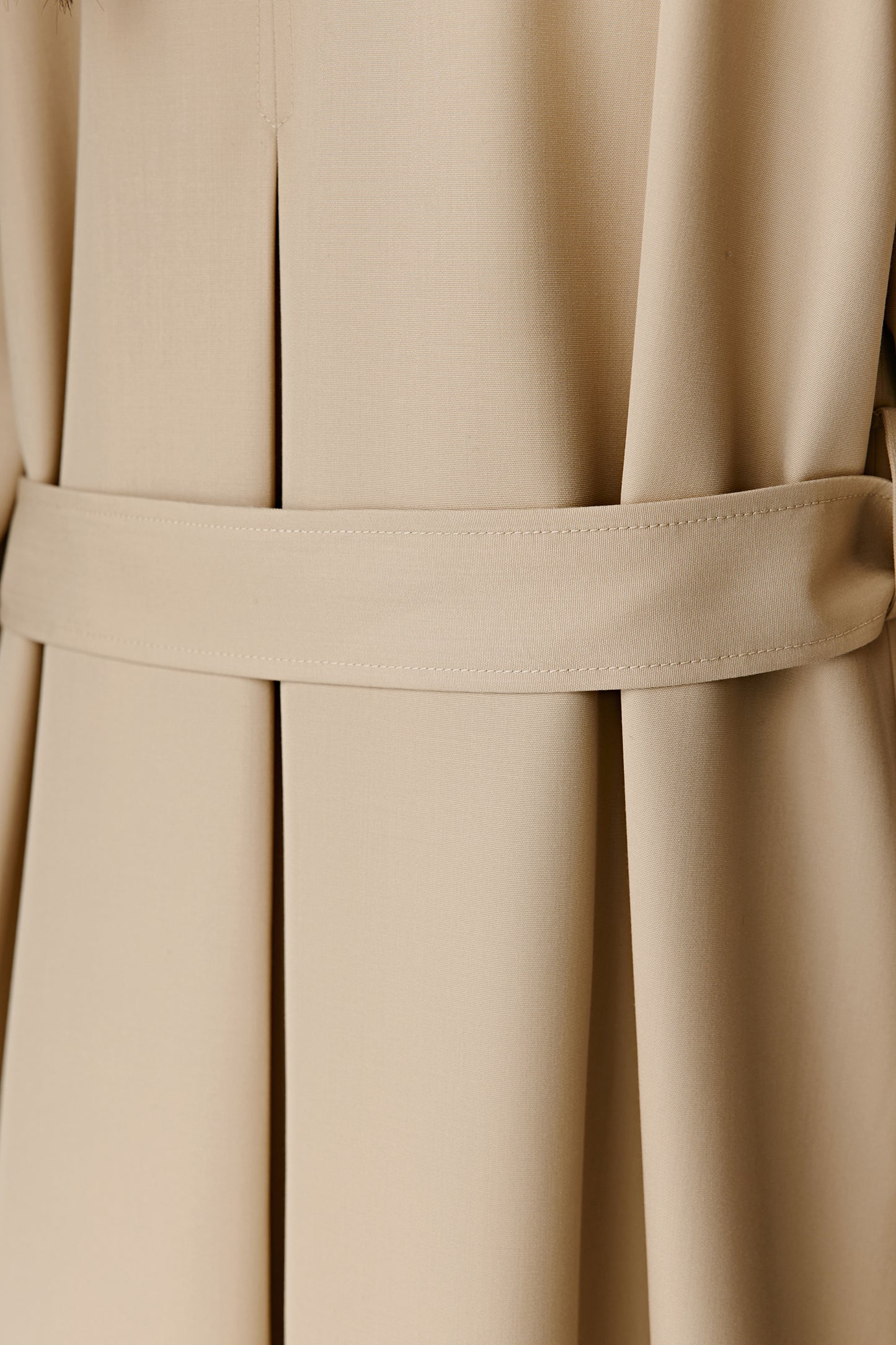Close-up of the back belt and pleated detail of a beige trench coat.