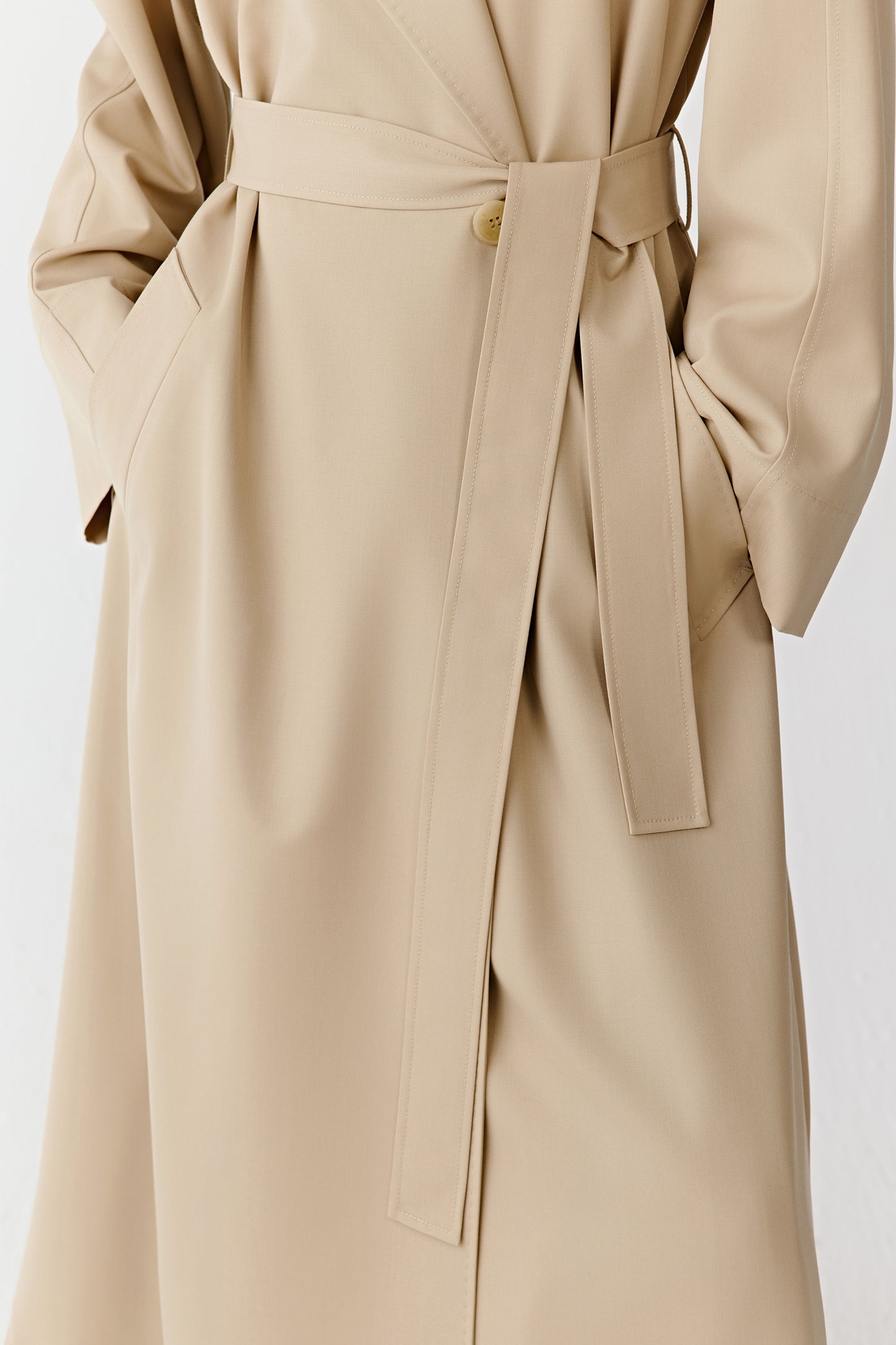 Detail of a beige trench coat showing the waist belt, side pocket, and button closure.