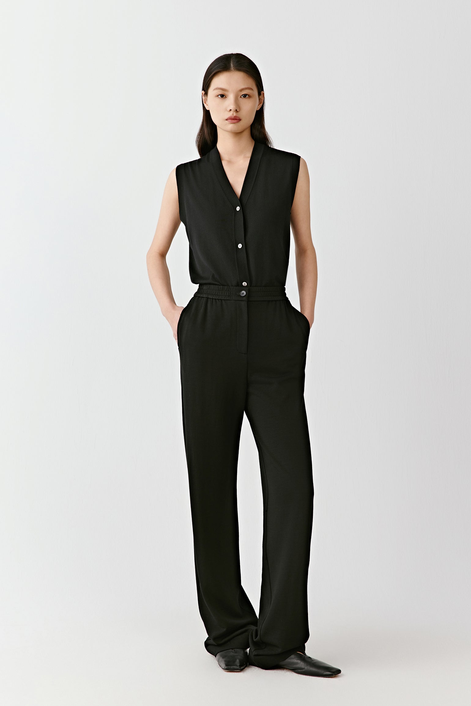 A woman wears deep black wool terry trousers paired with a sleeveless matching top, facing forward in a calm, neutral setting.