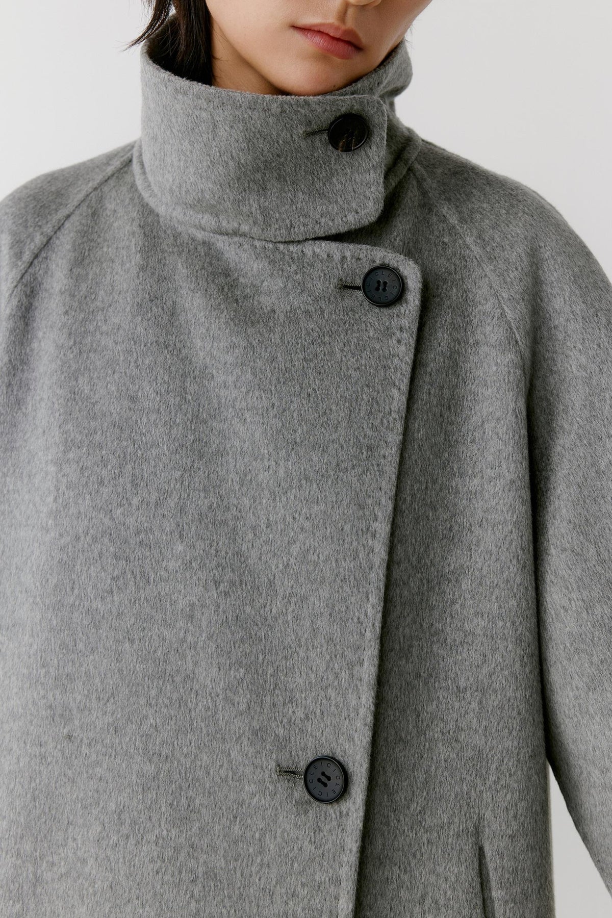 Close-up highlighting the high stand collar, asymmetric button fastening and soft grey melange cashmere surface.