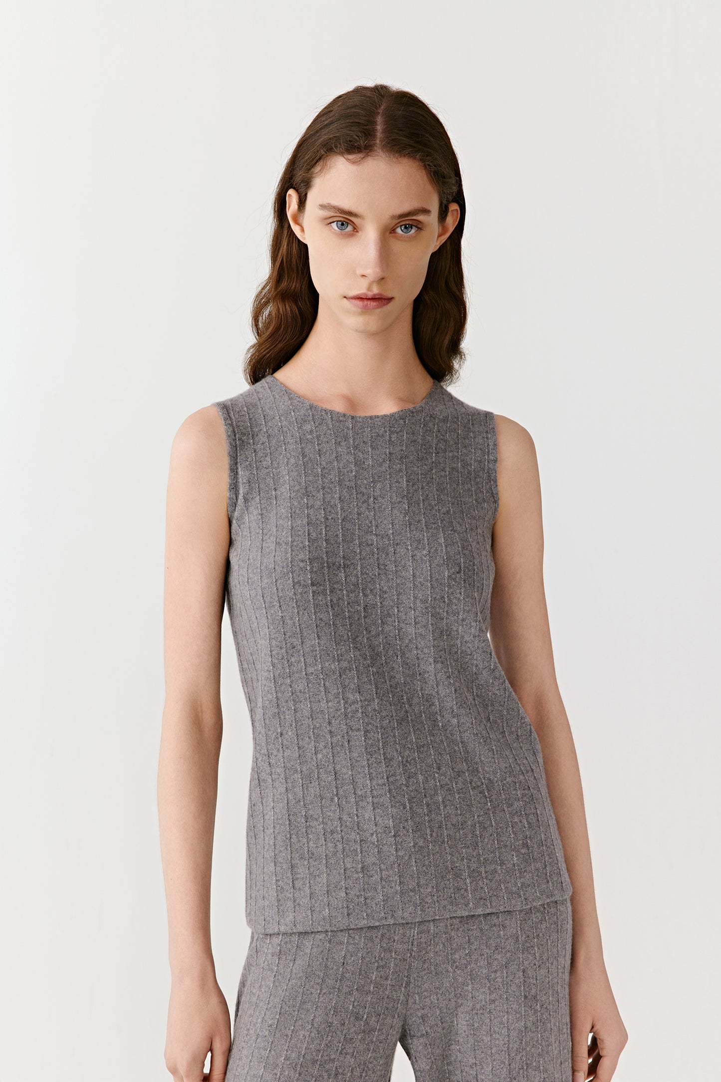 Front view of a woman wearing a light grey ribbed sleeveless top in wool and cashmere, styled with matching trousers.