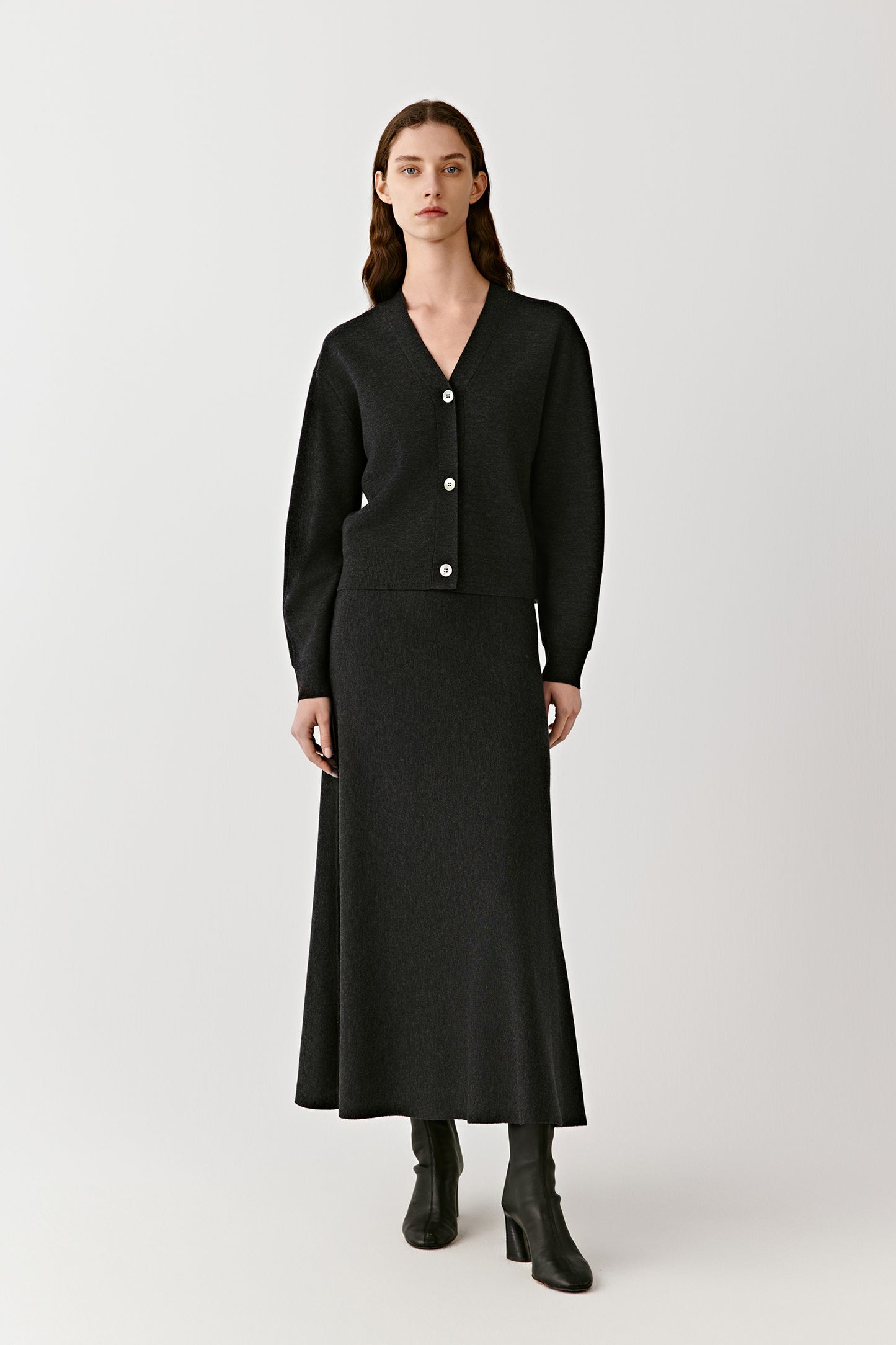 Woman wearing a long black button front knit skirt styled with a fitted black top on a light background