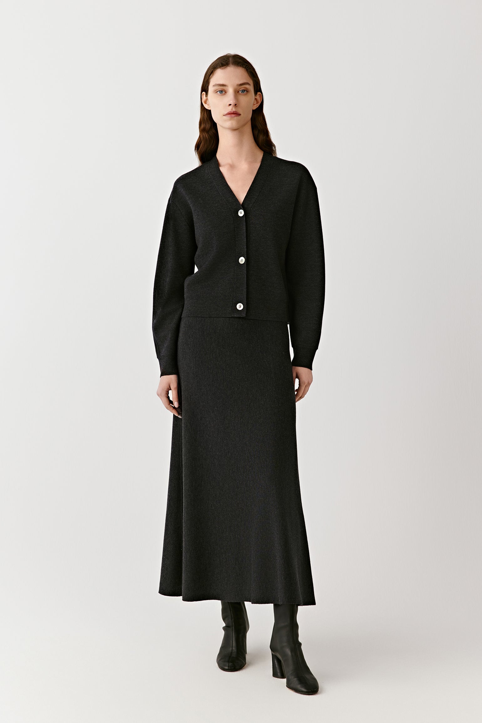 Woman wearing a long black button front knit skirt styled with a fitted black top on a light background