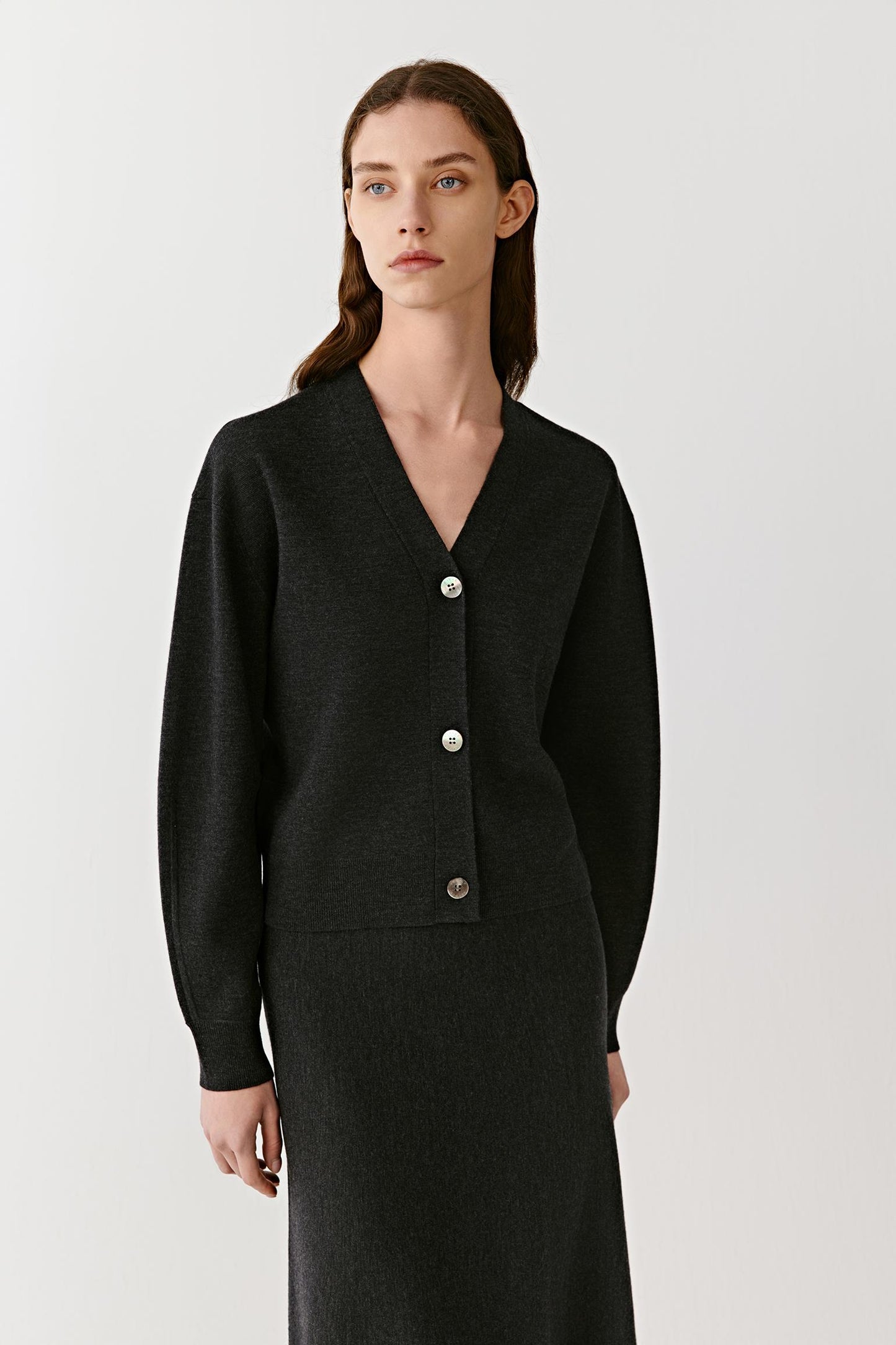 Front view of a woman wearing a black cashmere V-neck cardigan with a straight fit and large tonal buttons.