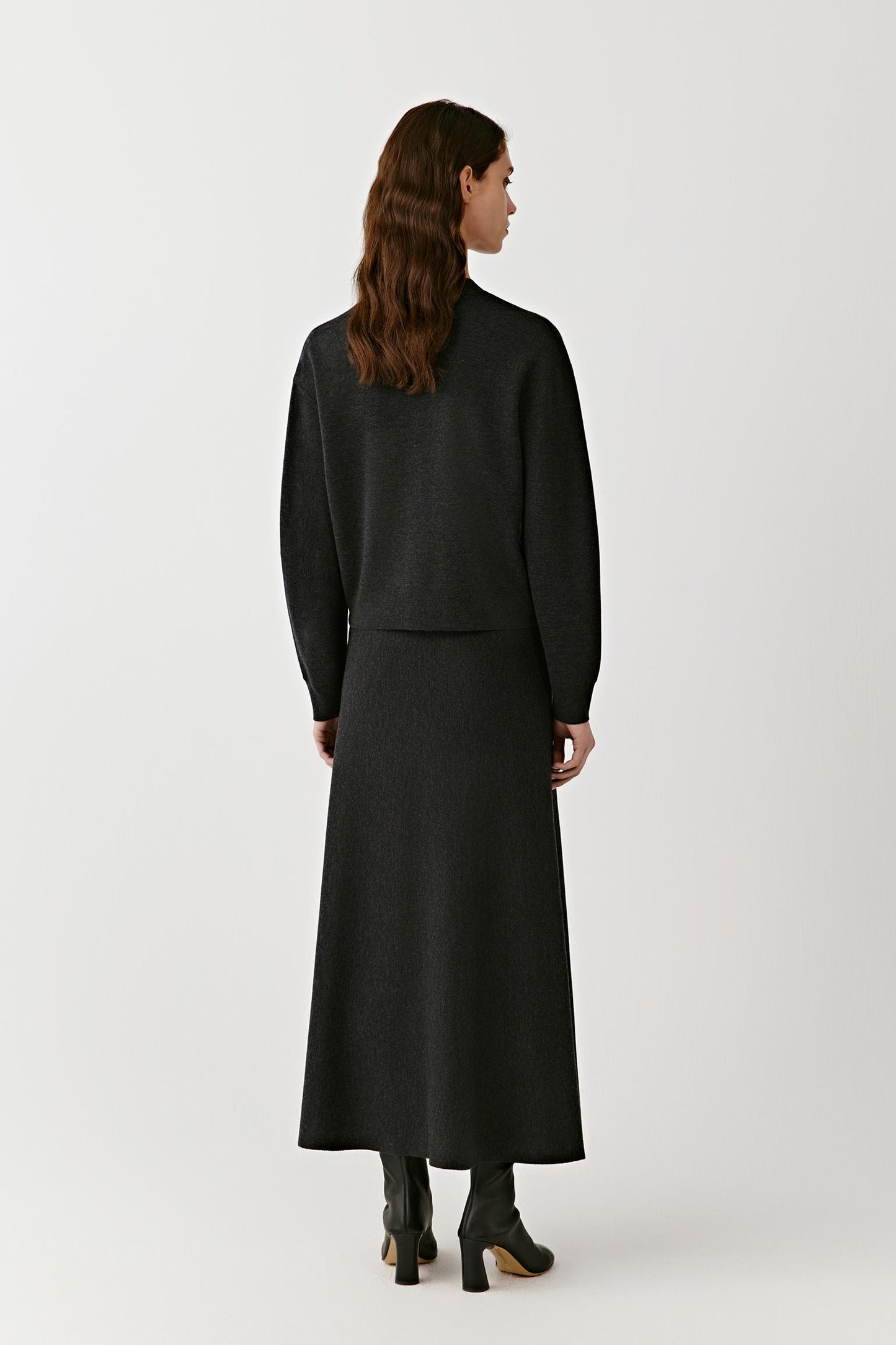 Full-length back view of a woman wearing the black V-neck cardigan layered over a long matching skirt.