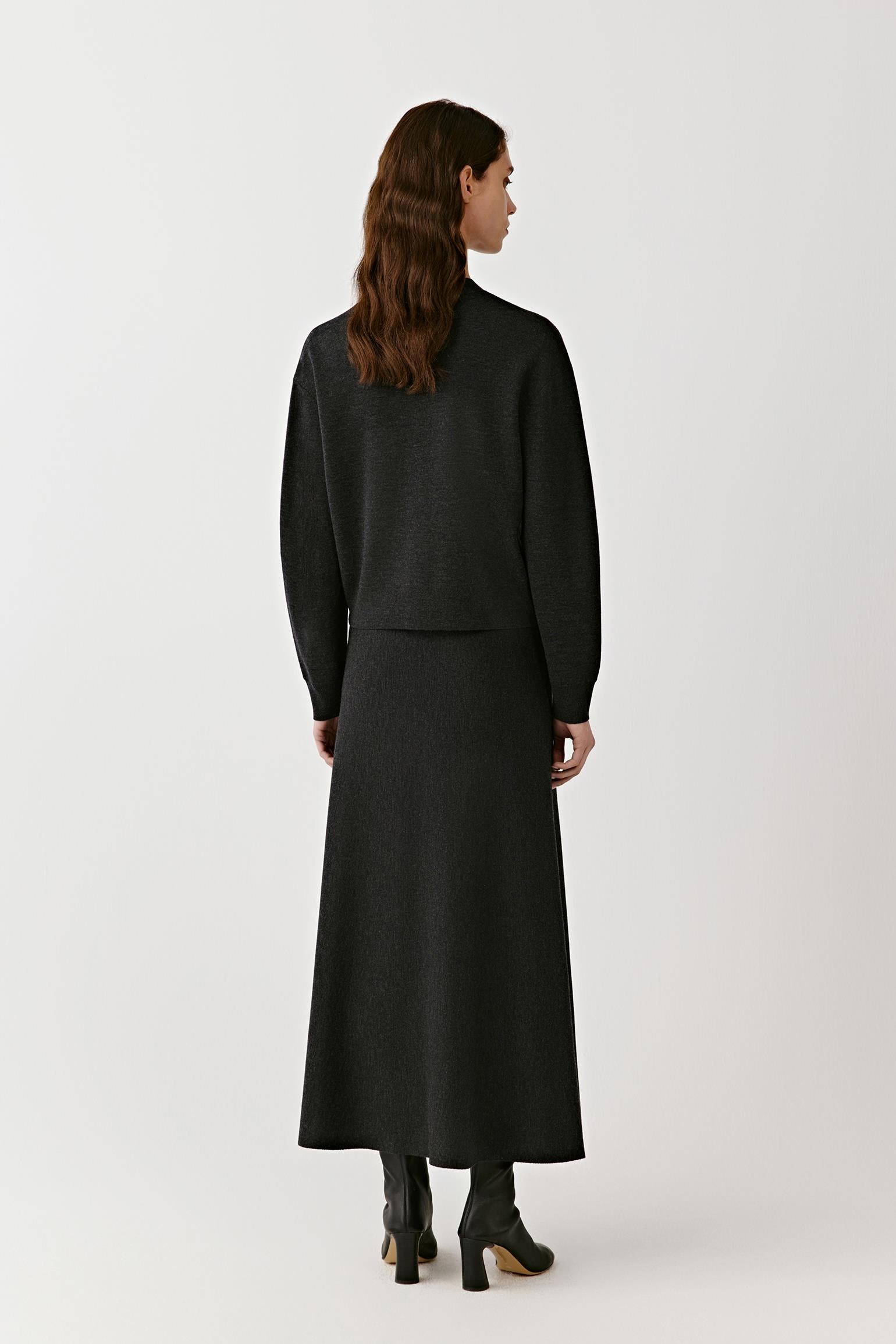 Full-length back view of a woman wearing the black V-neck cardigan layered over a long matching skirt.