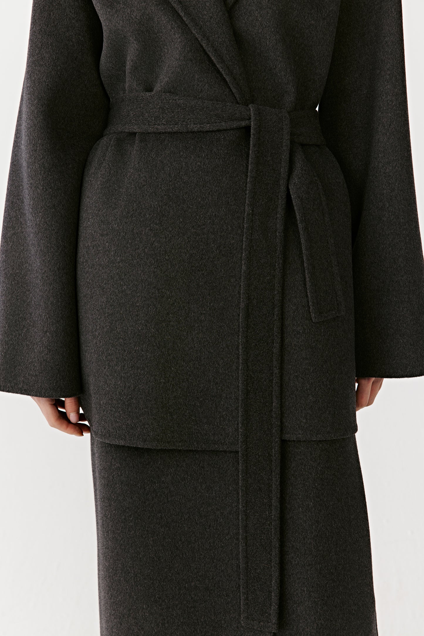Close-up of a black hooded wool coat collar and belted waist on a light background