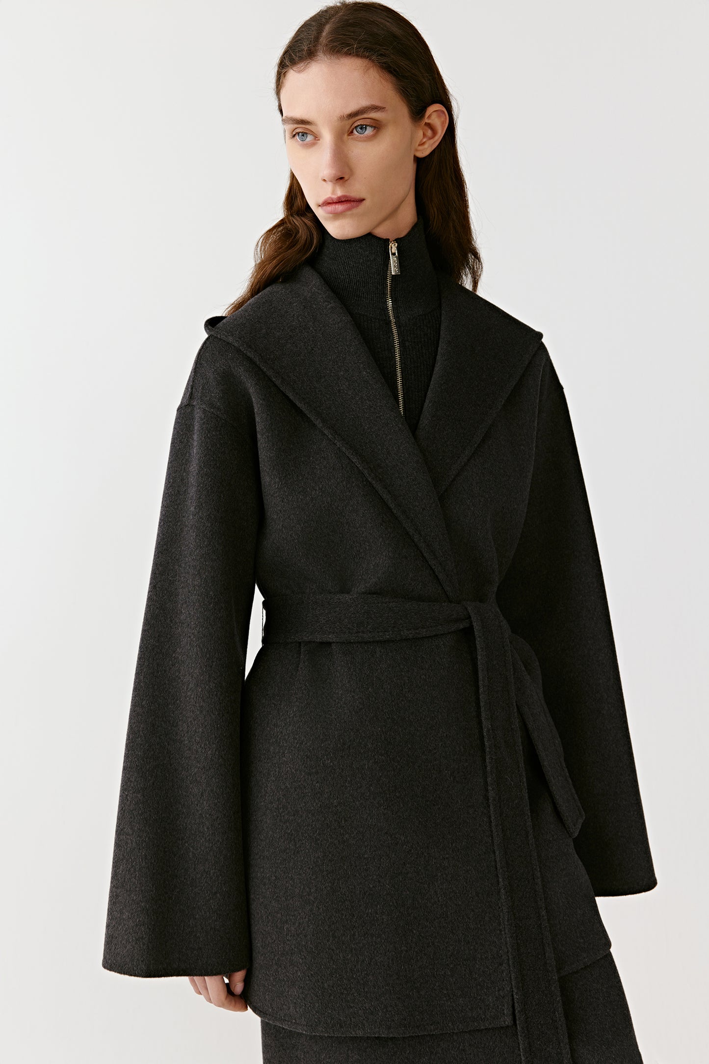 Close-up of a black hooded wool coat collar and belted waist on a light background
