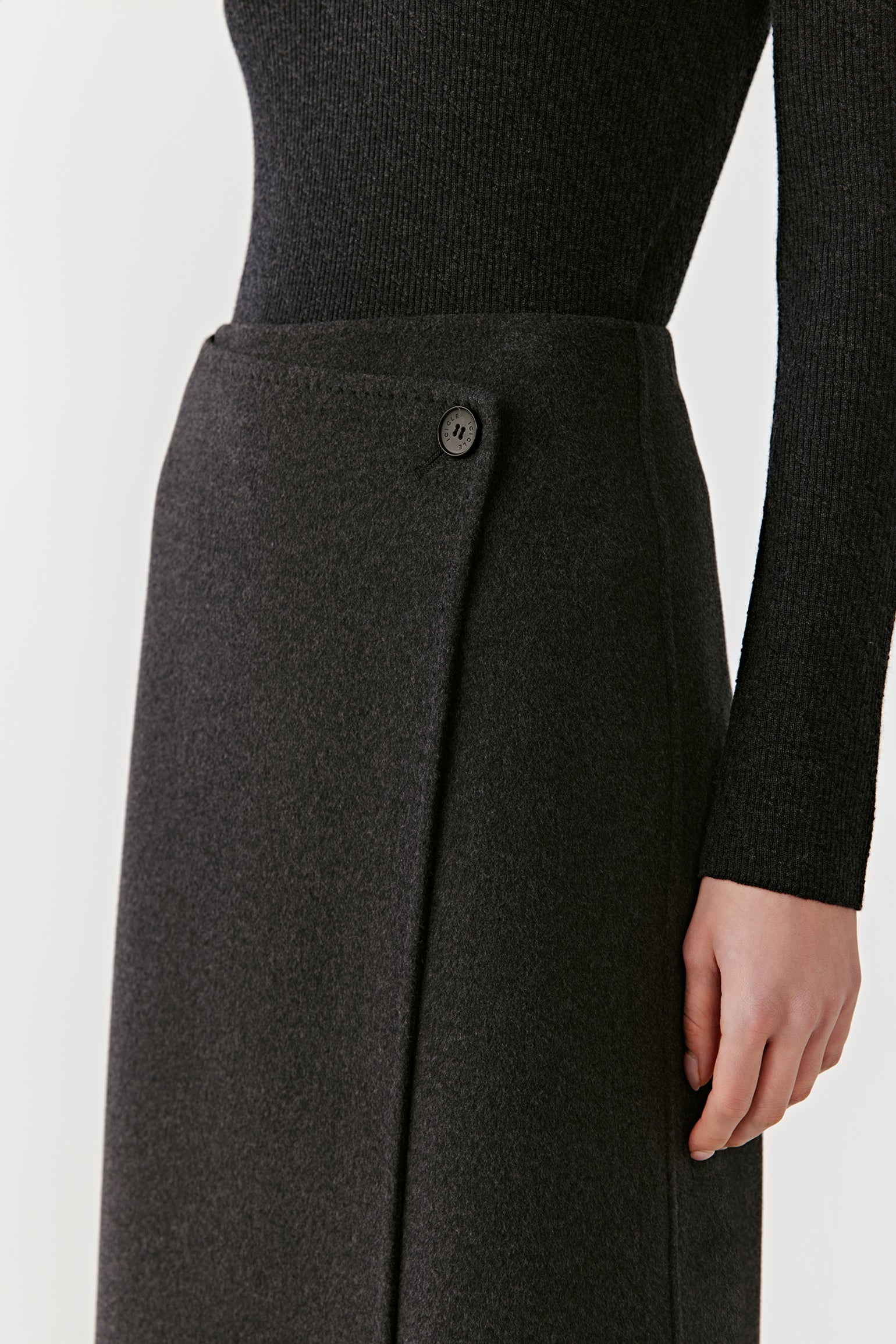 Close-up of the waistline and wrap fastening of the dark grey skirt, showing textured wool fabric and a clean side closure.