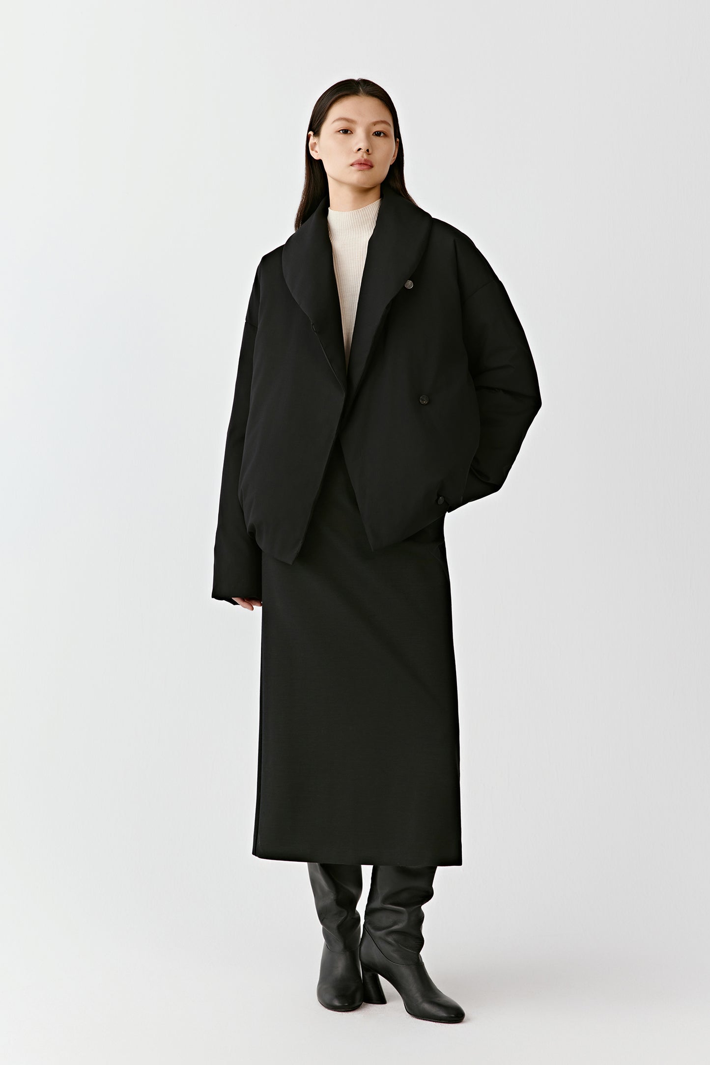 Front view of a woman wearing a short black double-faced wool and cashmere coat with wide lapels and a relaxed, oversized silhouette.