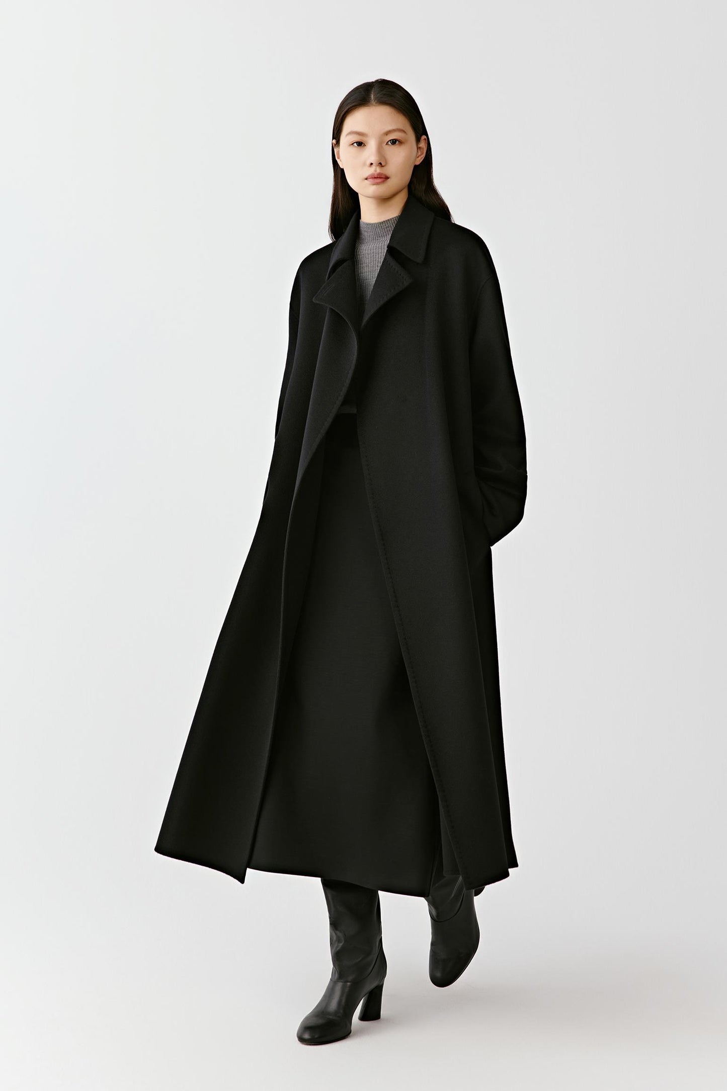Full body view of a long black wool coat with a tie belt on a light background