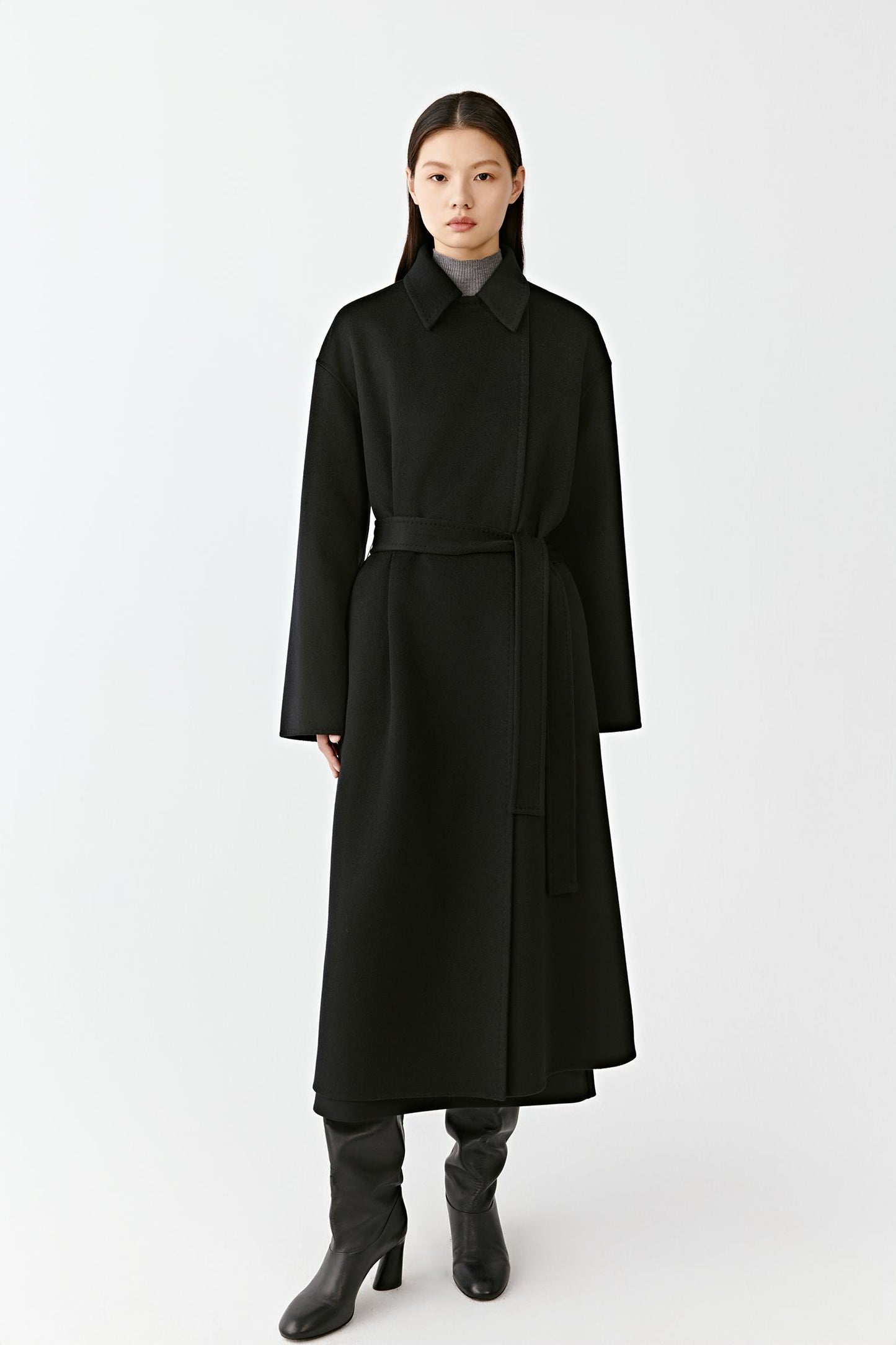 Woman wearing a long black wool coat with a belted waist on a light background