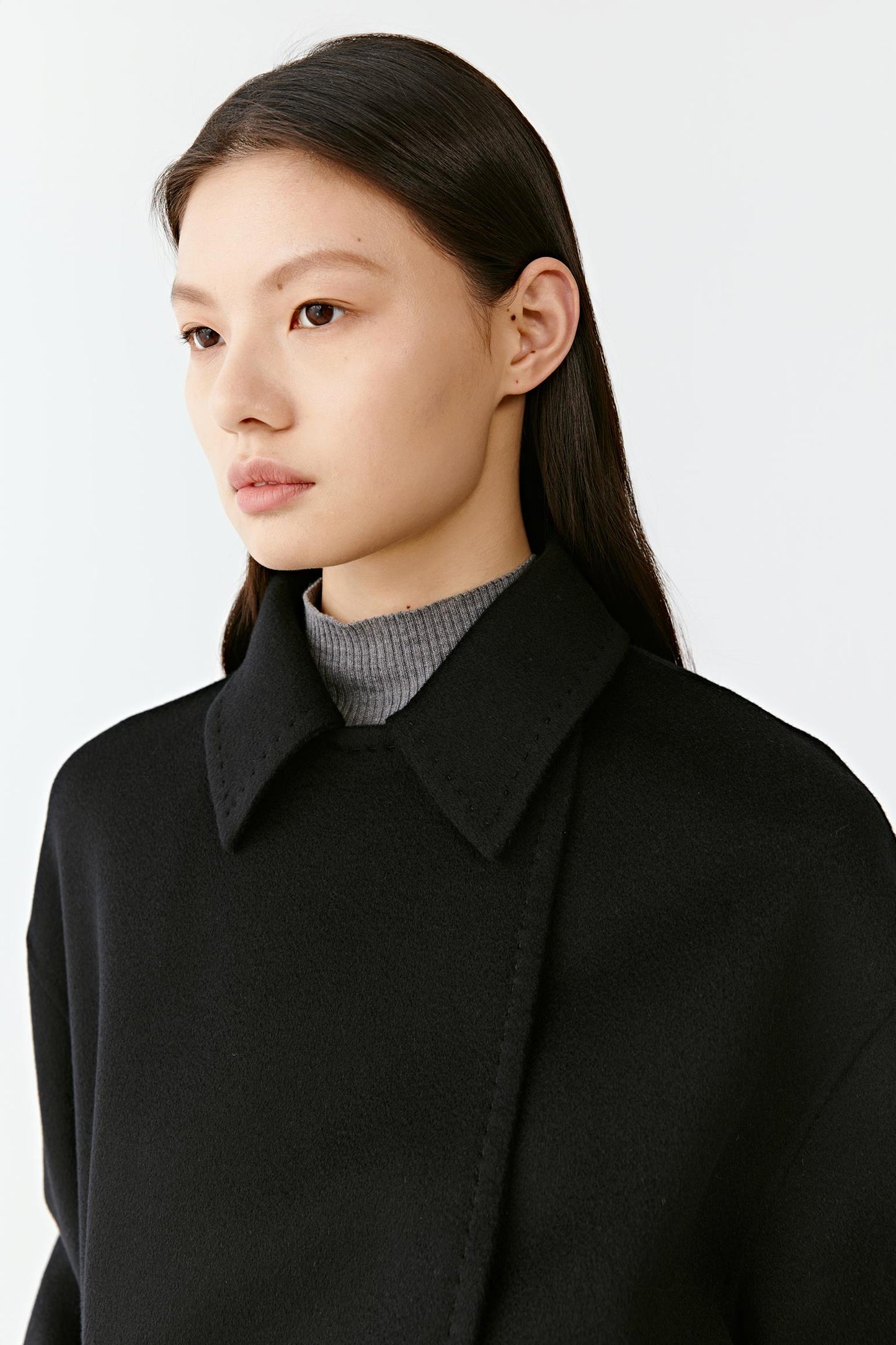 Close-up of a black wool coat collar and belted waist on a light background