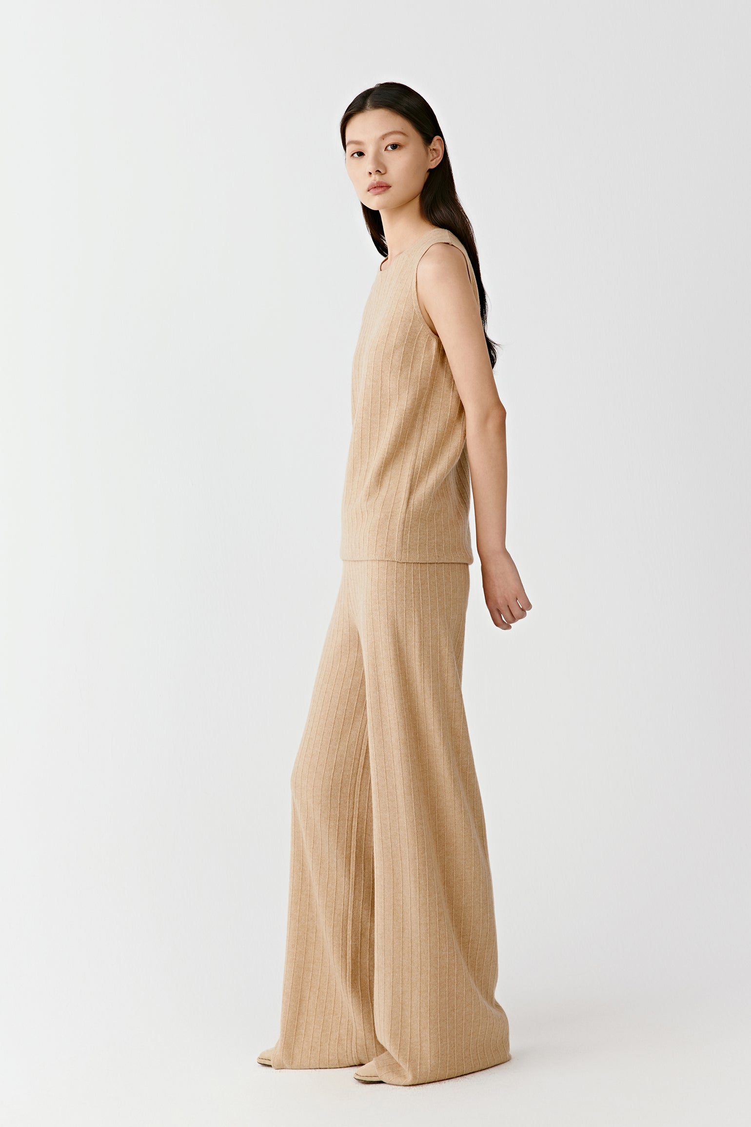 Woman wearing a sleeveless beige knit top with matching wide leg trousers on a light background
