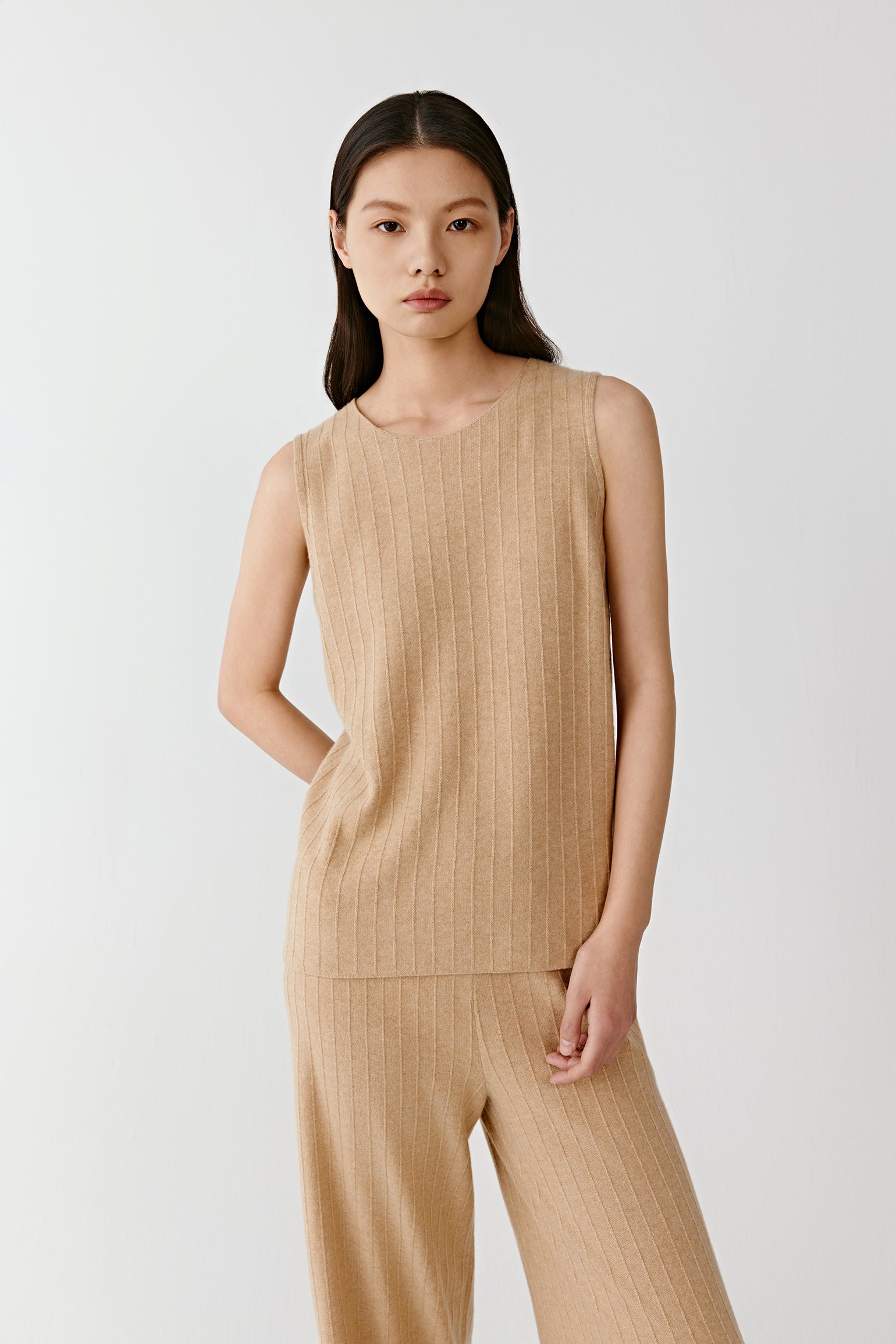 Woman wearing a sleeveless beige knit top styled with matching wide leg trousers on a light background
