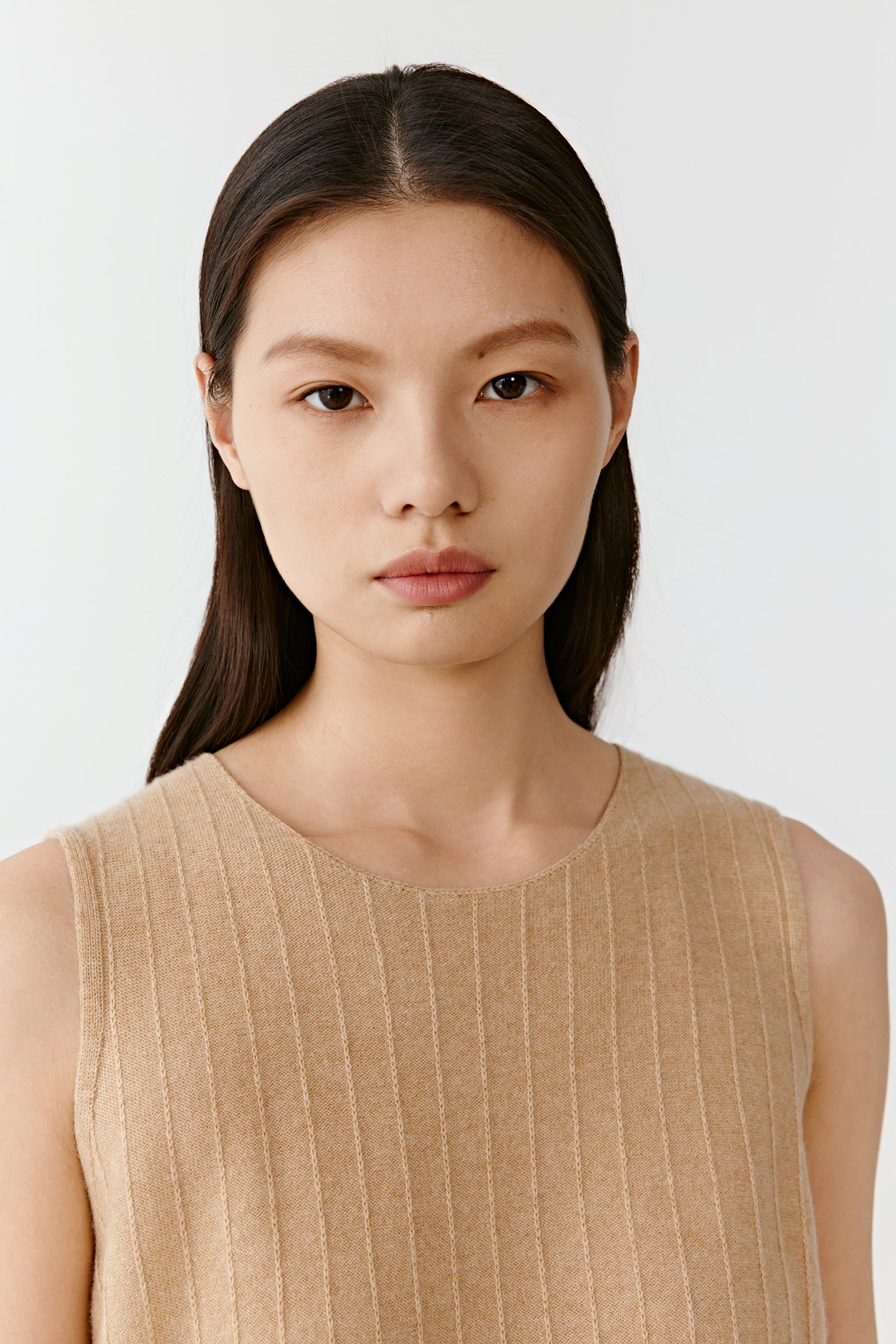 Close-up of a beige sleeveless knit top neckline on a light background